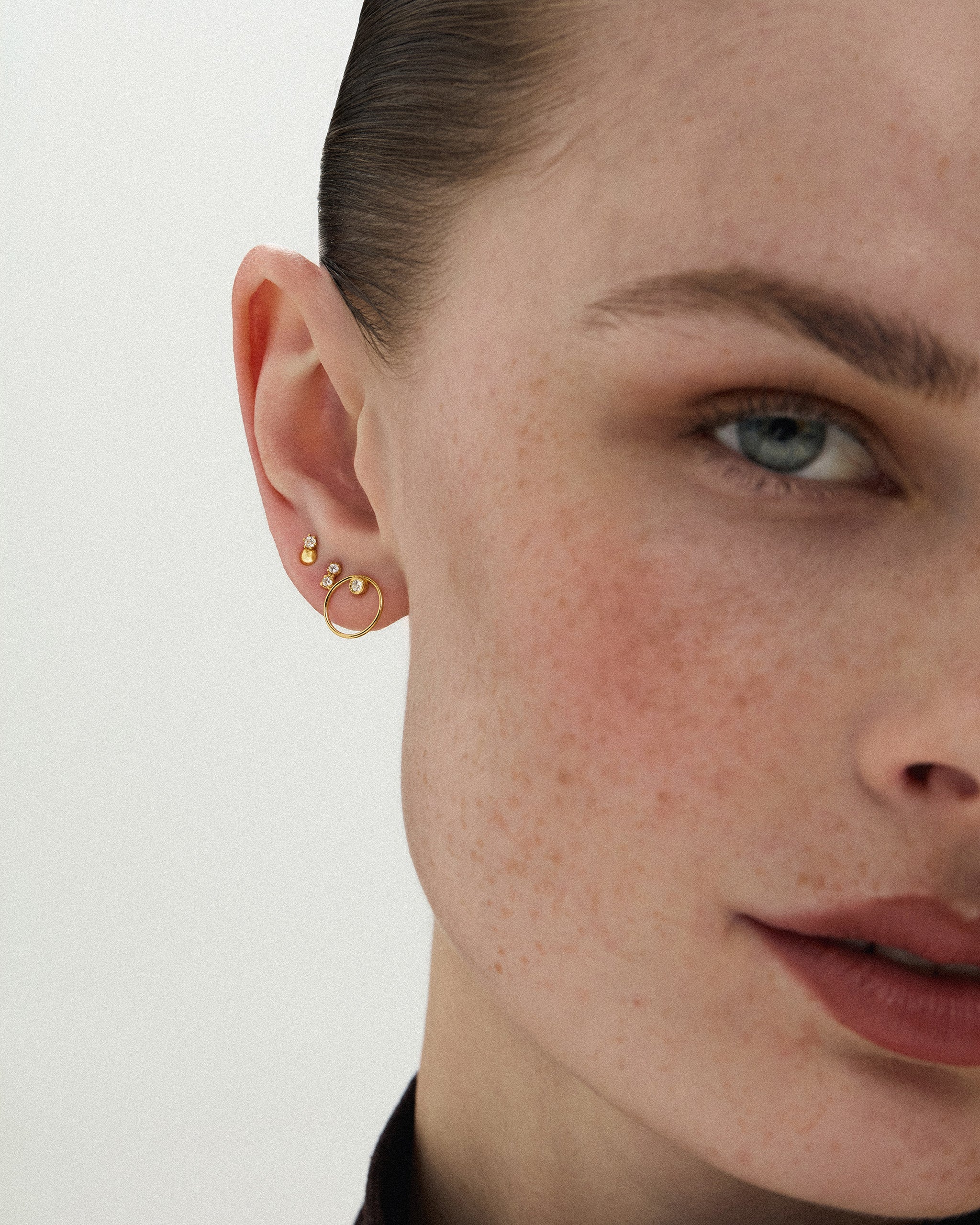 Woman wearing the Dyo Diamond Bead Studs in 14k yellow gold styled with a small gold hoop earring in a curated ear stack. ENEA Studio