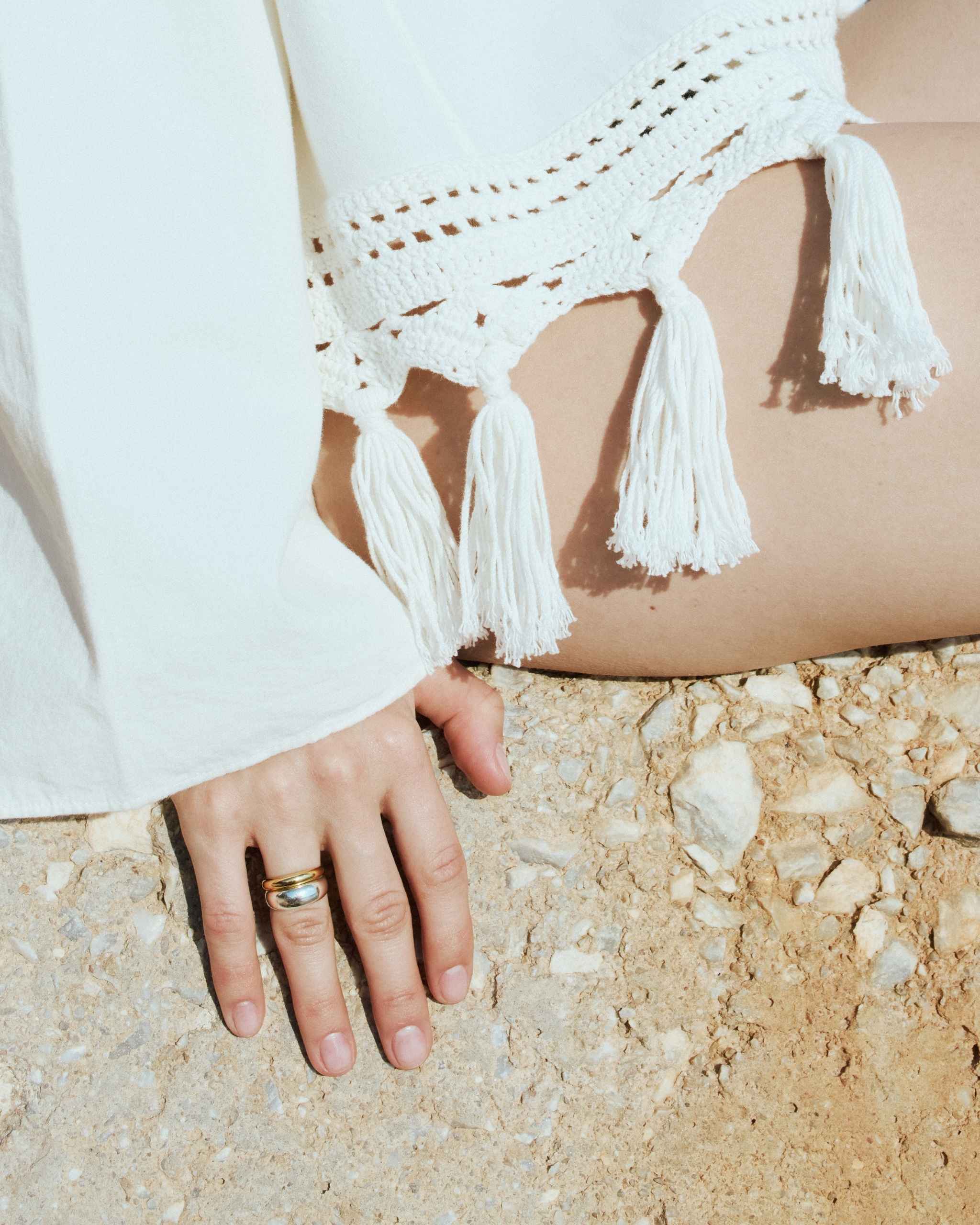 A woman's hand on textured soil styled with the DYO Dome Stacking Ring set, 14k gold and sterling silver