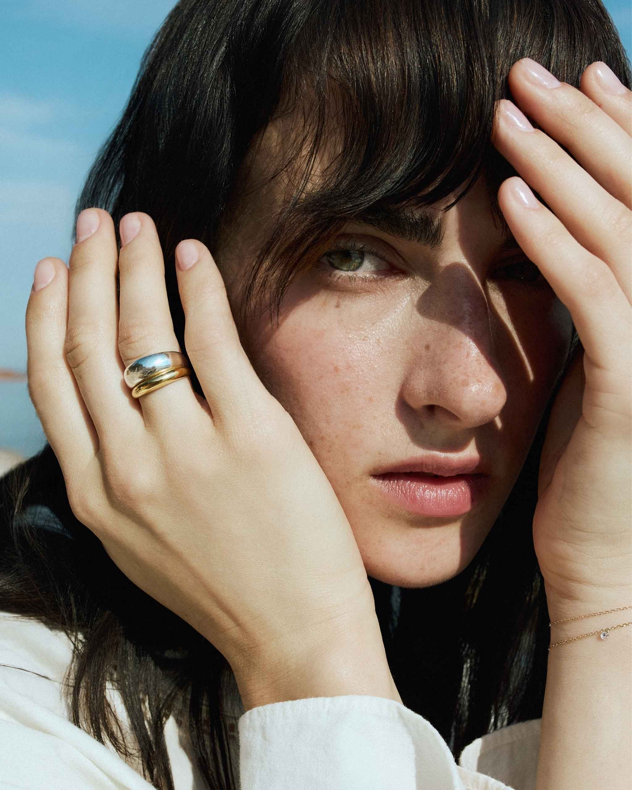 Model wears the DYO Dome Stacking Ring set, 14k gold and sterling silver, close crop on hand near face.