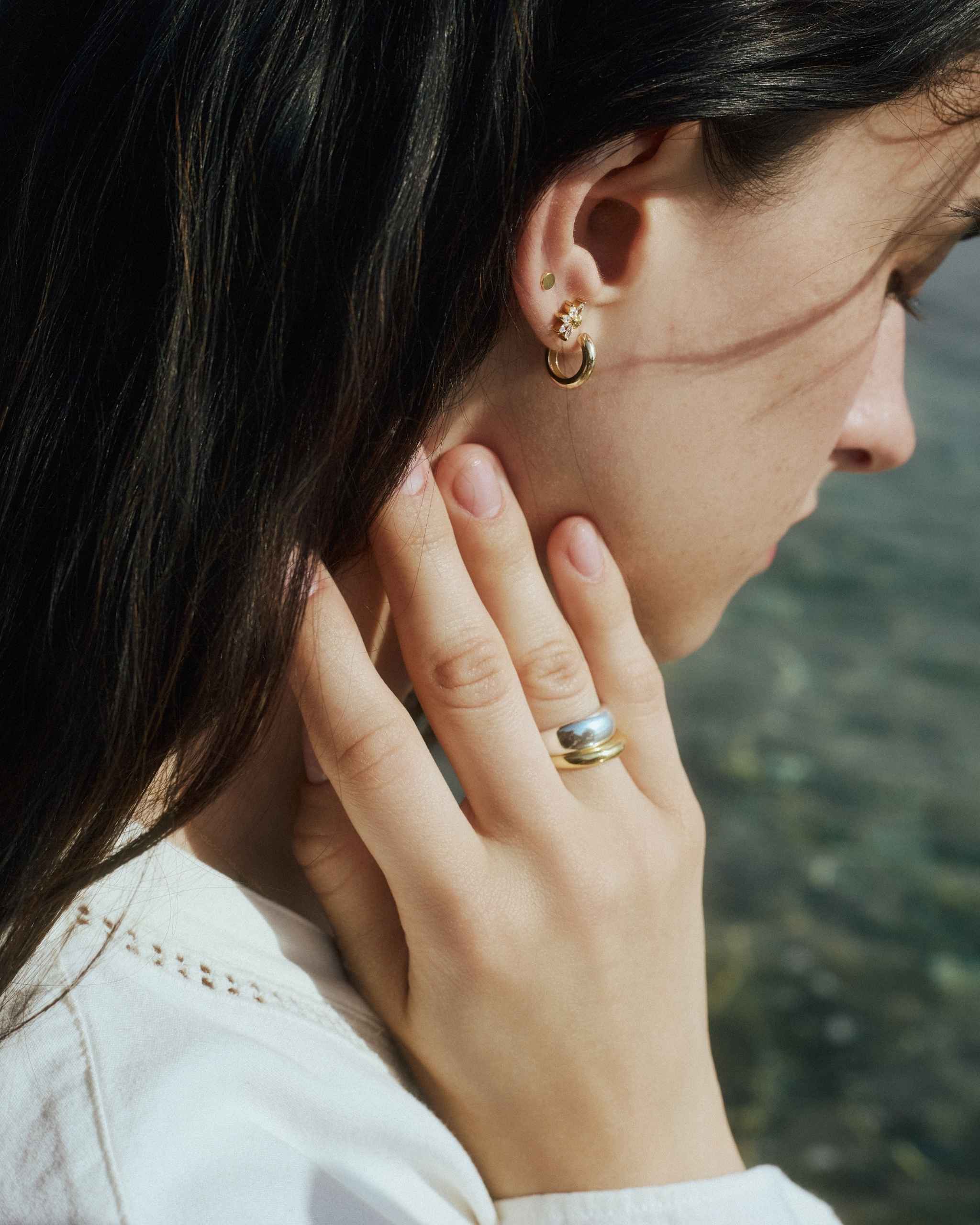Model wears a small gold hoop and delicate gold and diamond studs, styled with the DYO Dome Stacking Ring set in 14k gold and sterling silver, close crop on hand near face.