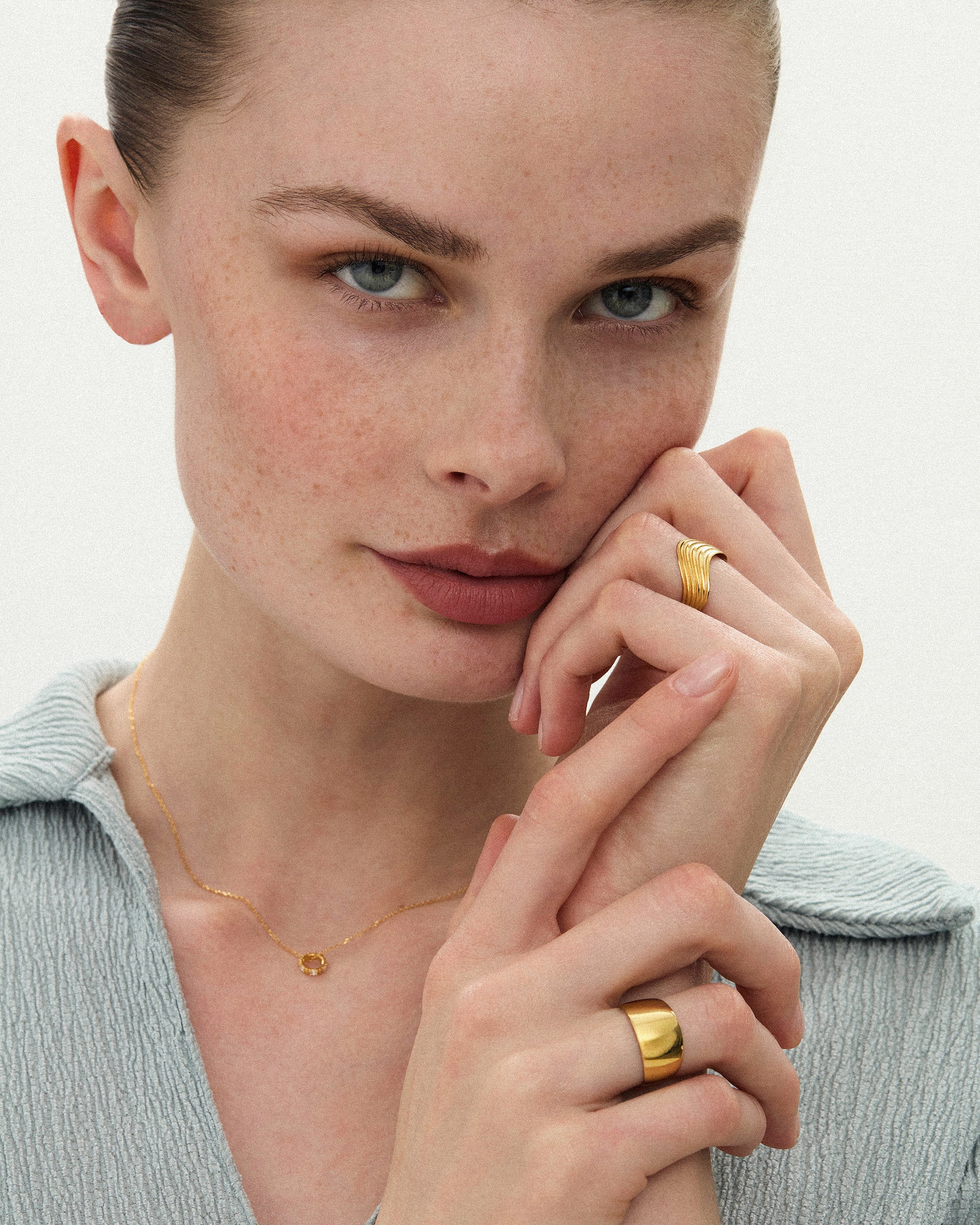 Woman against a blurred background wearing the Kion III Ribbed Wave Ring and Cigar Band in solid yellow gold