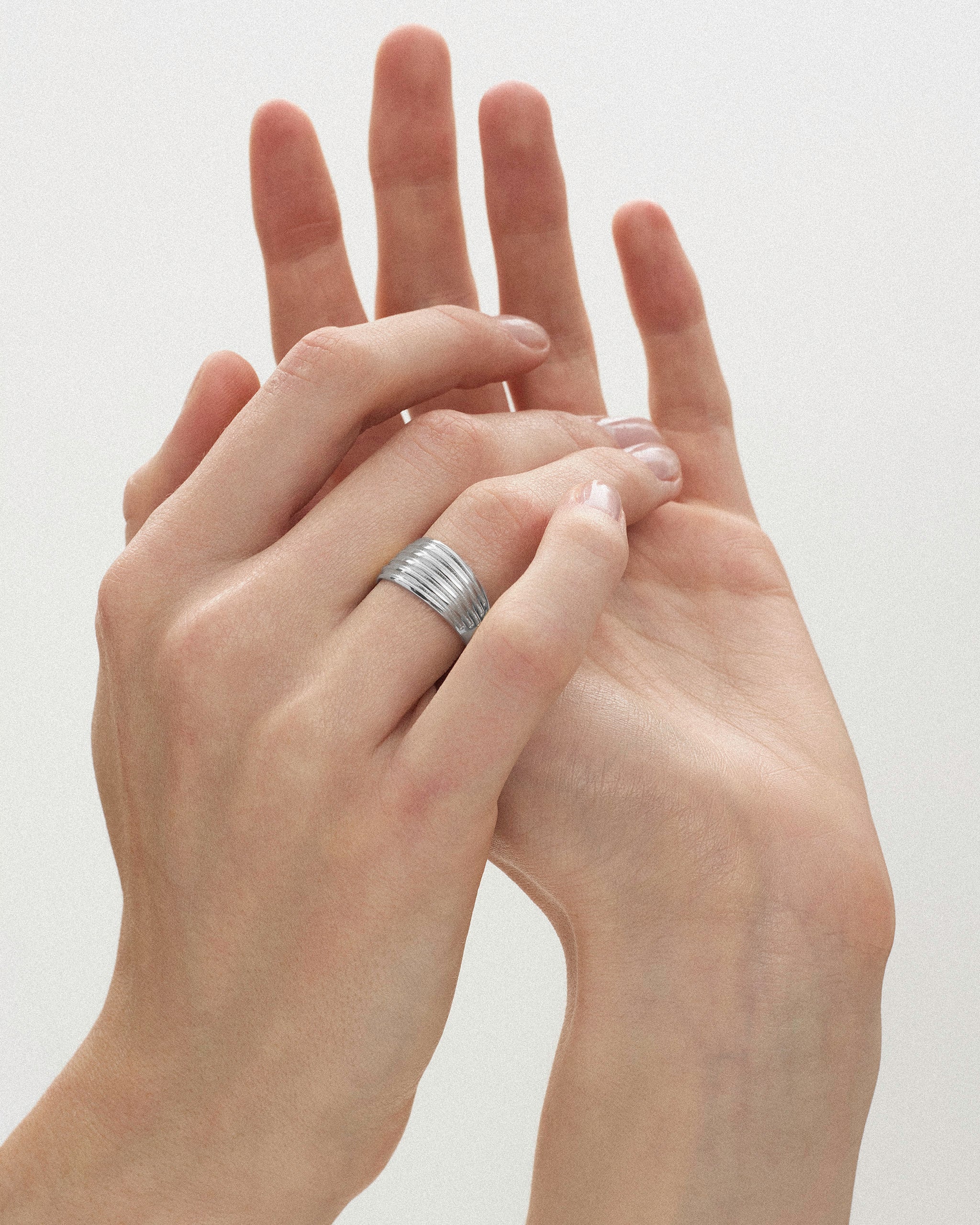 Close-up of a woman's hands styled with the Kíon II Ribbed Band Ring in sterling silver y ENEA