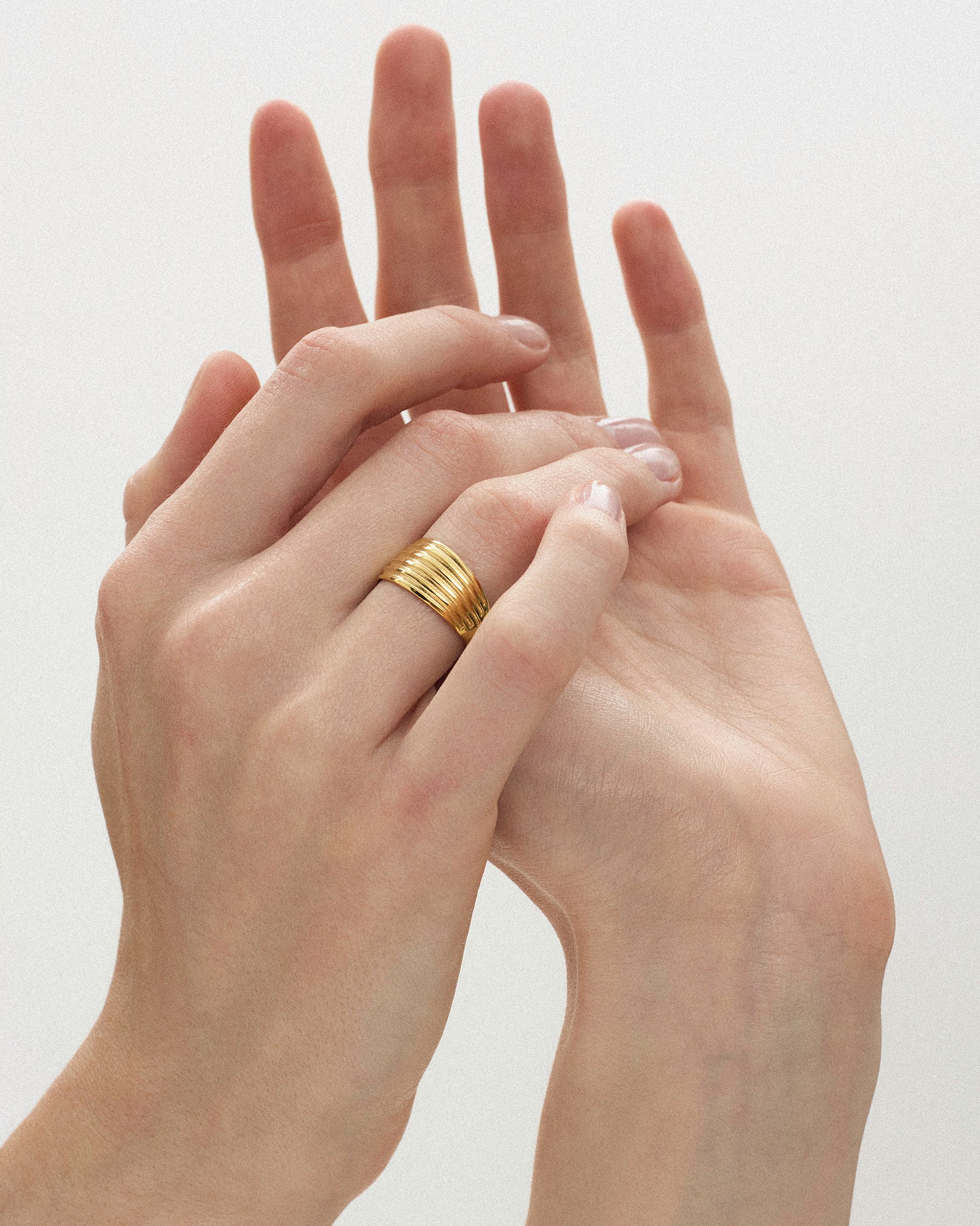 Close-up of a woman's hands styled with the Kíon II Ribbed Band Ring in solid yellow gold by ENEA