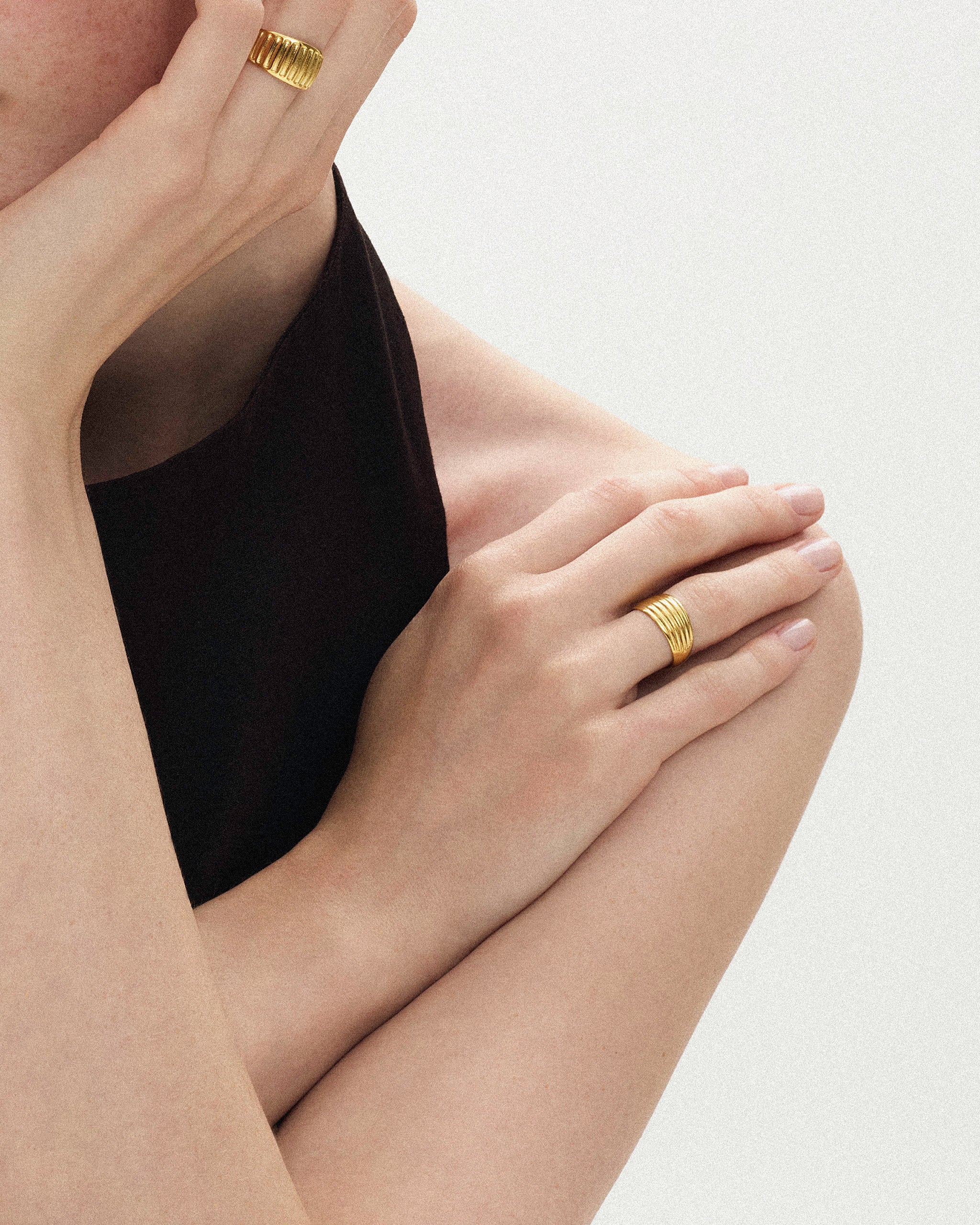 Woman in brown blouse wearing a thick ribbed yellow gold band on each hand against a soft beige background
