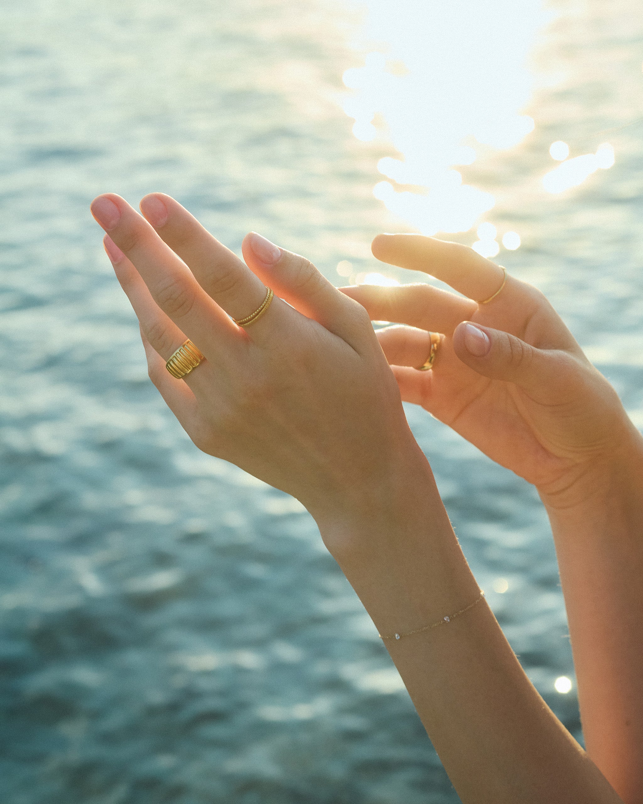 A sunlit close-up of hands with gold rings against a blurred water background