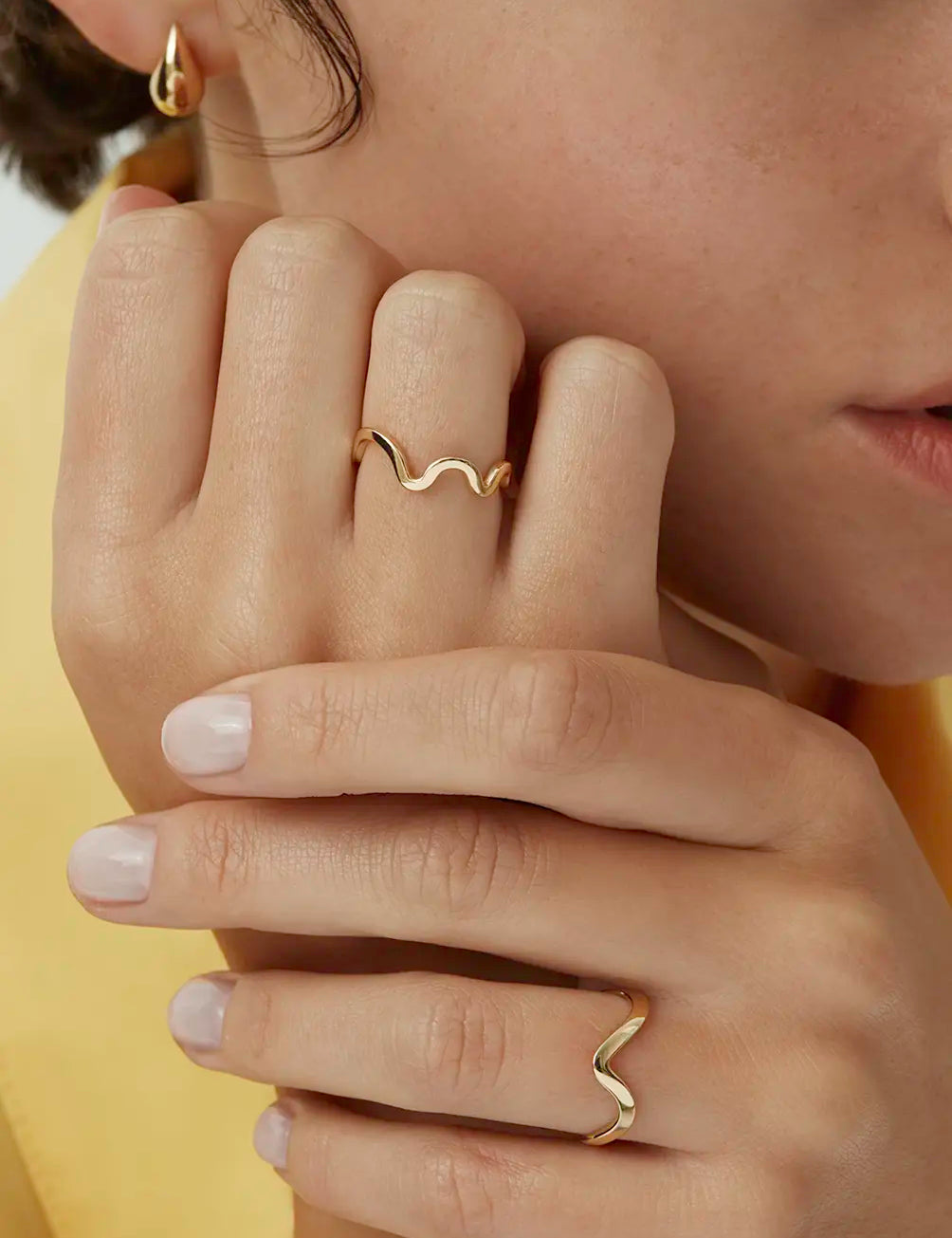 Close up of a model wearing the yellow gold Kyma Rhythm band ring styled with another wavy band - Enea Studio