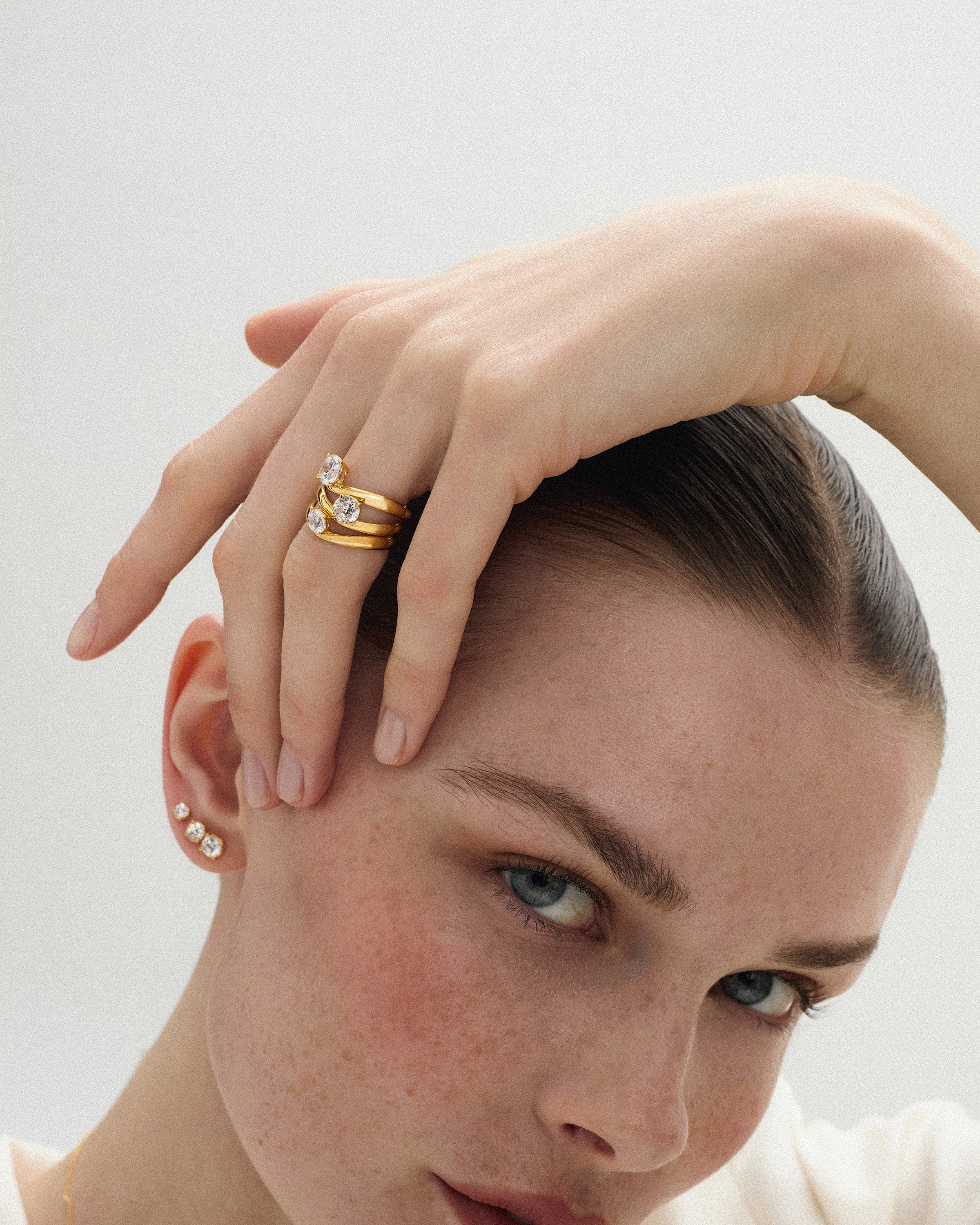 front view of a woman with her hand above her head wearing the kyma solitaire rings in solid yellow gold in 0.50ct, 0.75ct and 1ct sizes on a white background