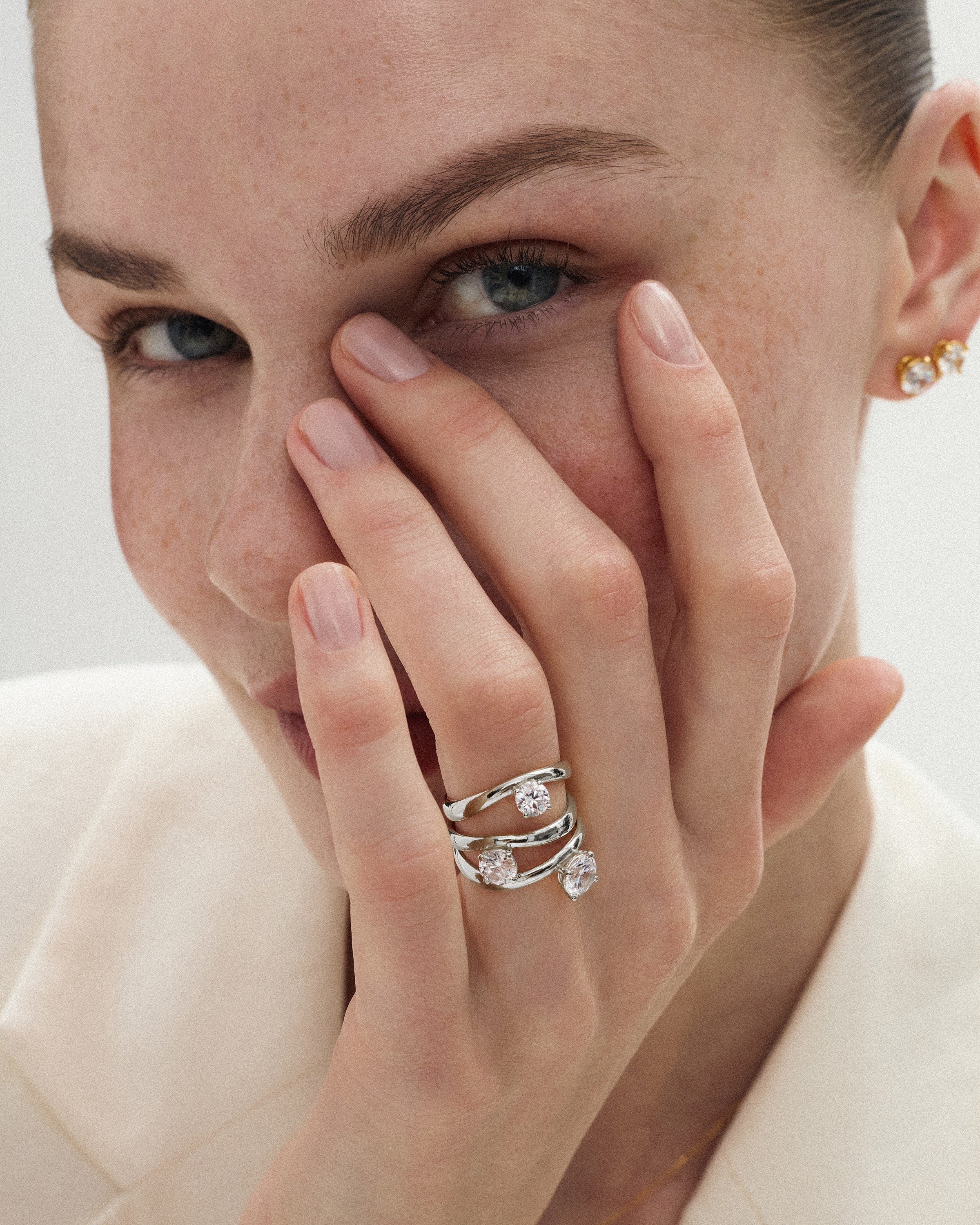angled view of a woman touching her face with her hand wearing the kyma solitaire rings in solid white gold in 0.50ct, 0.75ct and 1ct sizes on a white background