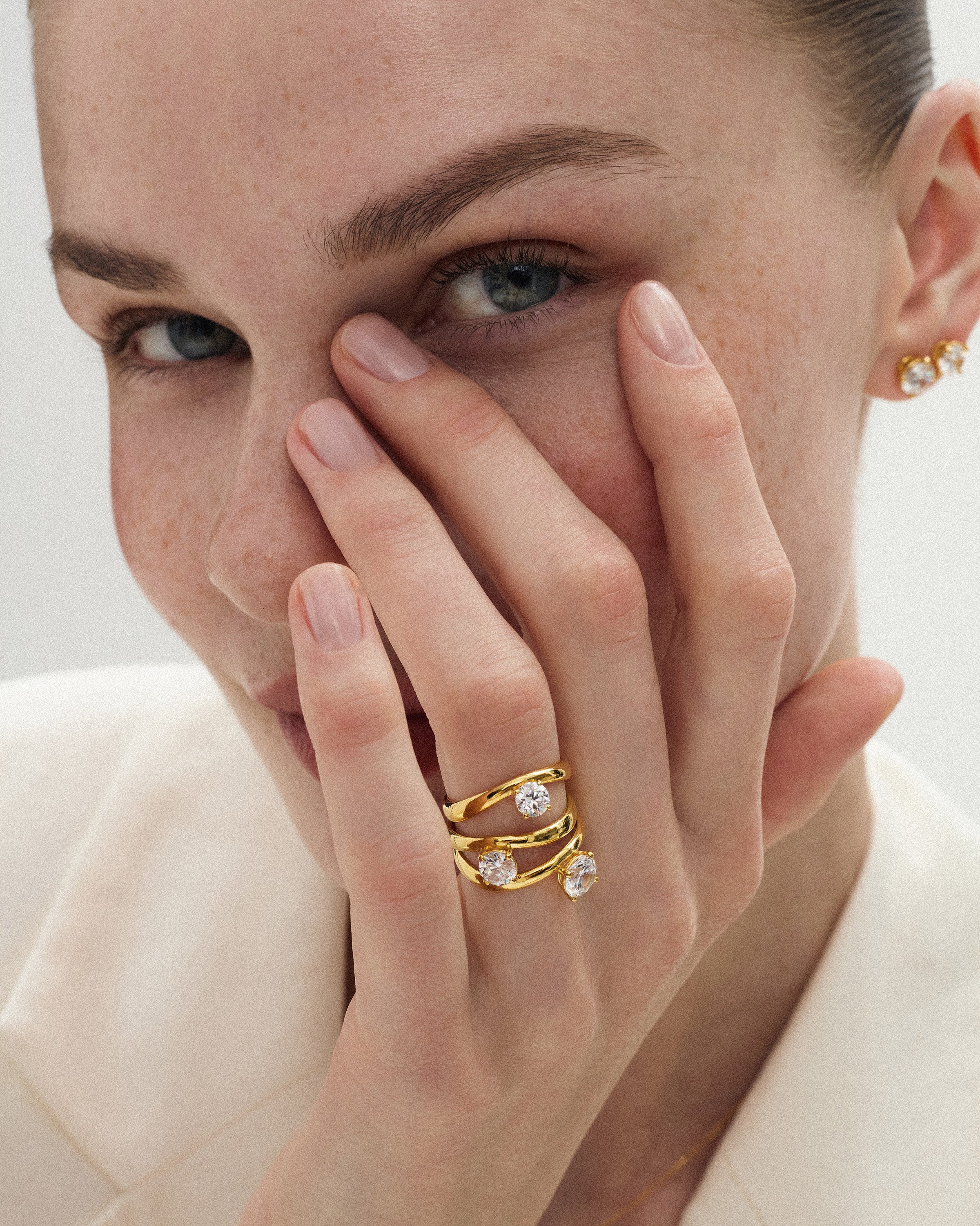 angled view of a woman touching her face with her hand wearing the kyma solitaire rings in solid yellow gold in 0.50ct, 0.75ct and 1ct sizes on a white background