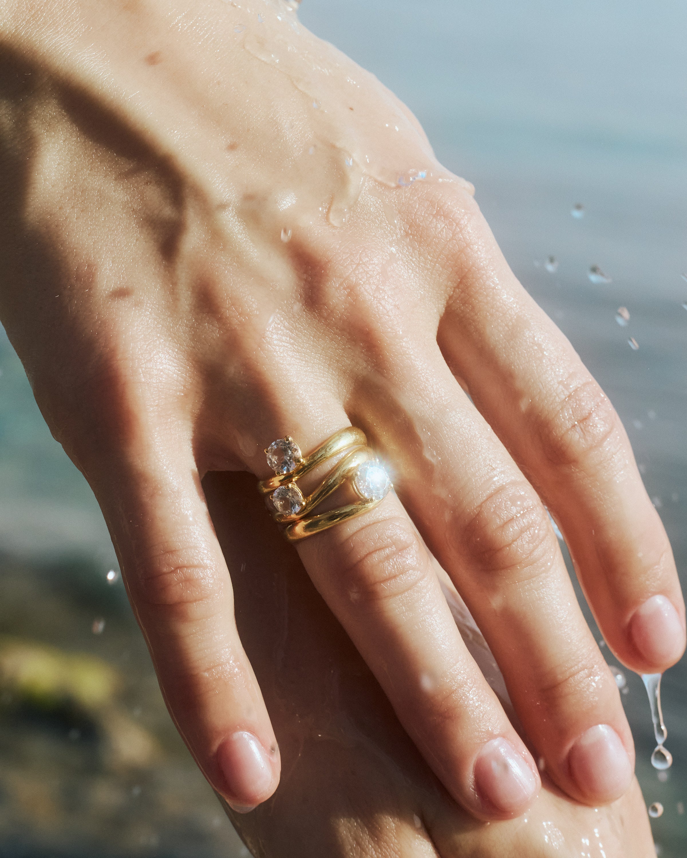 close up of a woman's hand wearing the kyma solitaire rings in solid yellow gold in 0.50ct, 0.75ct and 1ct sizes on a sea background