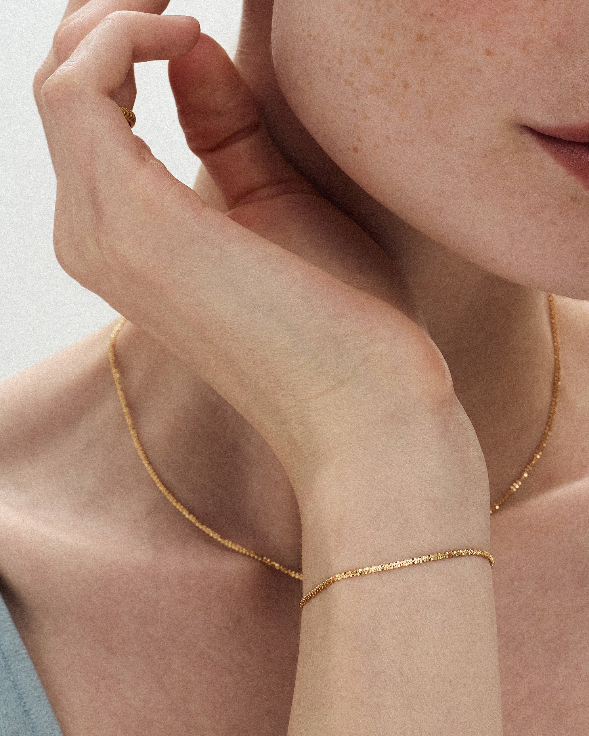 Close up of a woman wearing the Lumière Sparkle Chain Necklace in 14k yellow gold with a matching sparkle chain bracelet, hand raised to her chin. ENEA Studio
