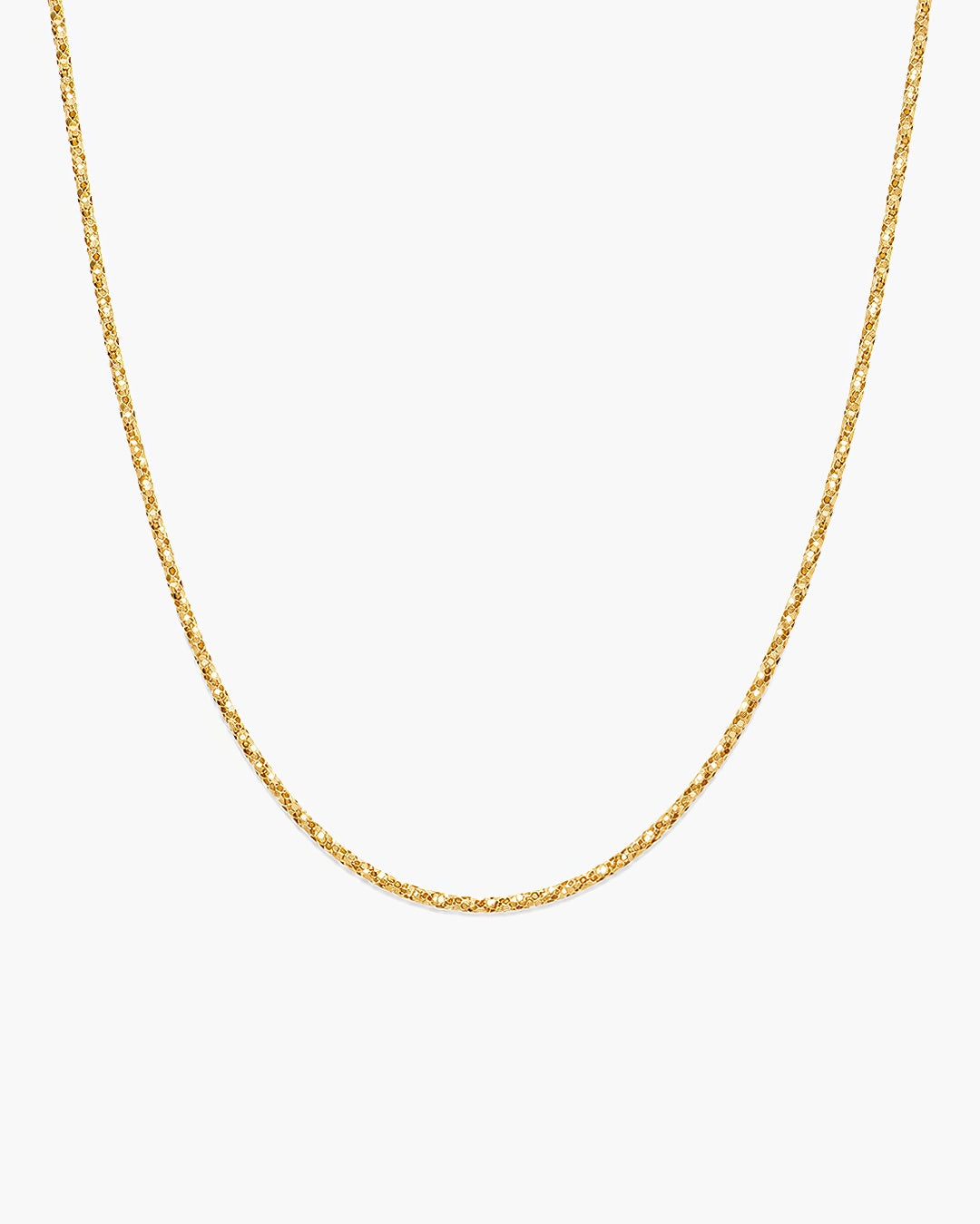 Lumière Sparkle Chain Necklace in 14k yellow gold, a diamond cut chain with faceted links catching light, on an off-white surface. ENEA Studio