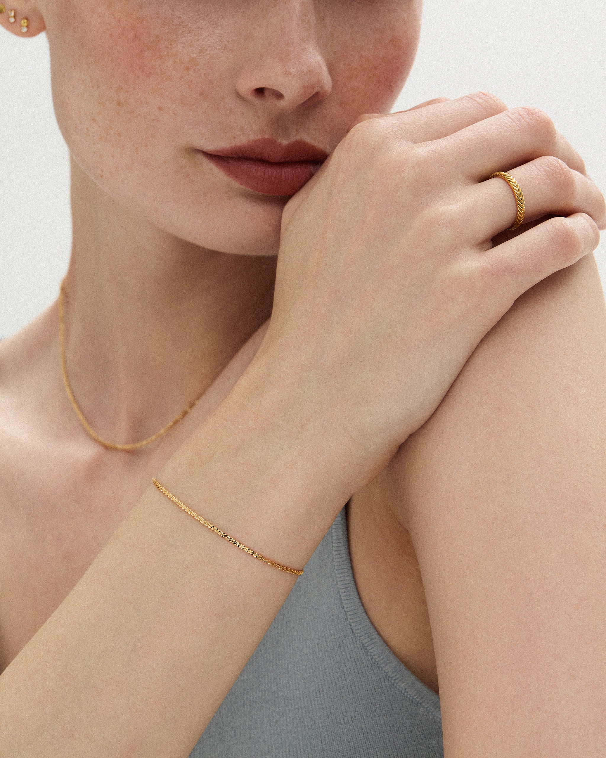 Woman wearing the Lumière Sparkle Chain Bracelet in 14k yellow gold on her wrist with the matching Lumière Sparkle Chain Necklace at her collarbone, hand at her chin. ENEA Studio