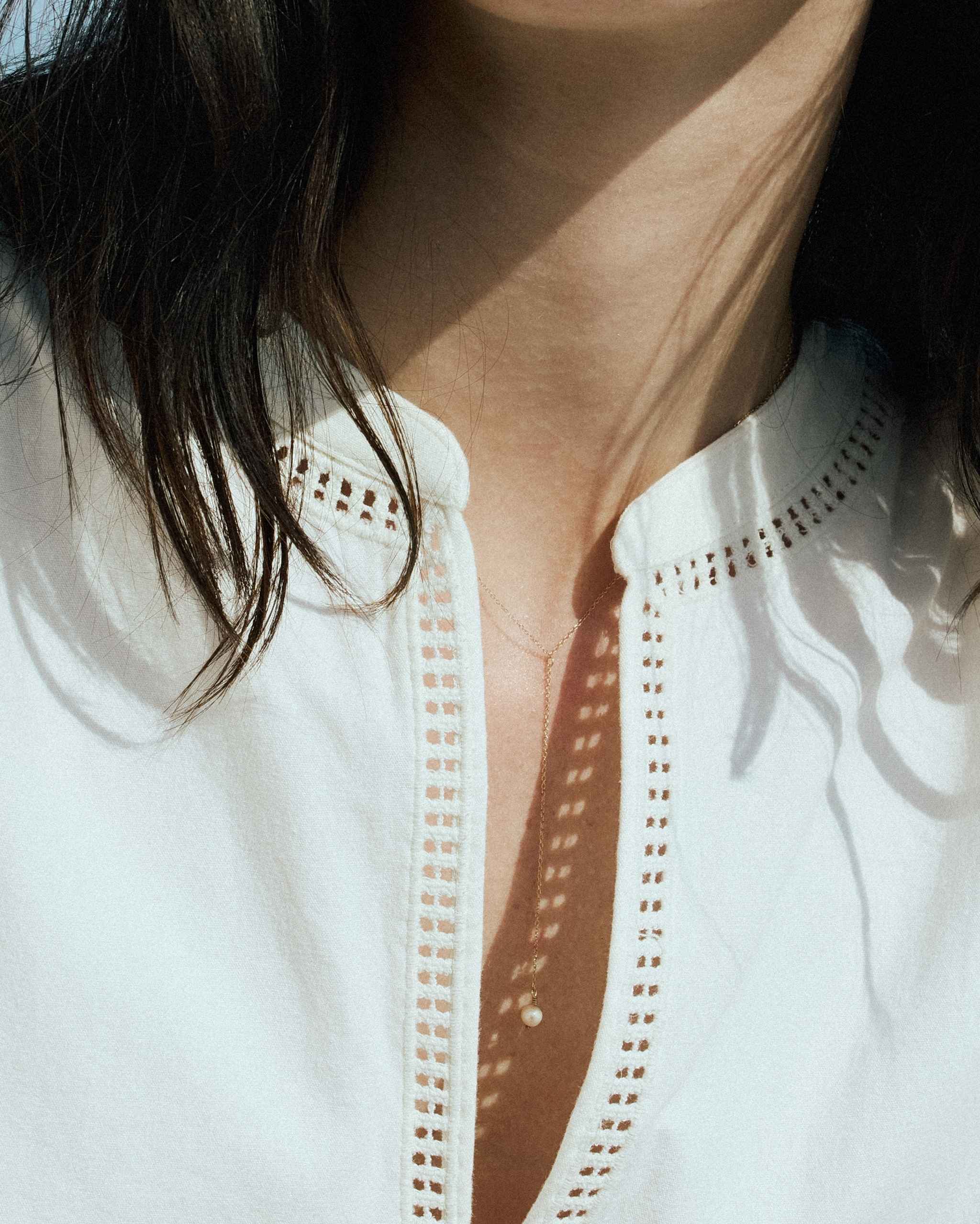 close up of a woman in white shirt wearing  a 14k yellow gold lariat pearl necklace showing freshwater pearl drop pendant on gold chain necklace