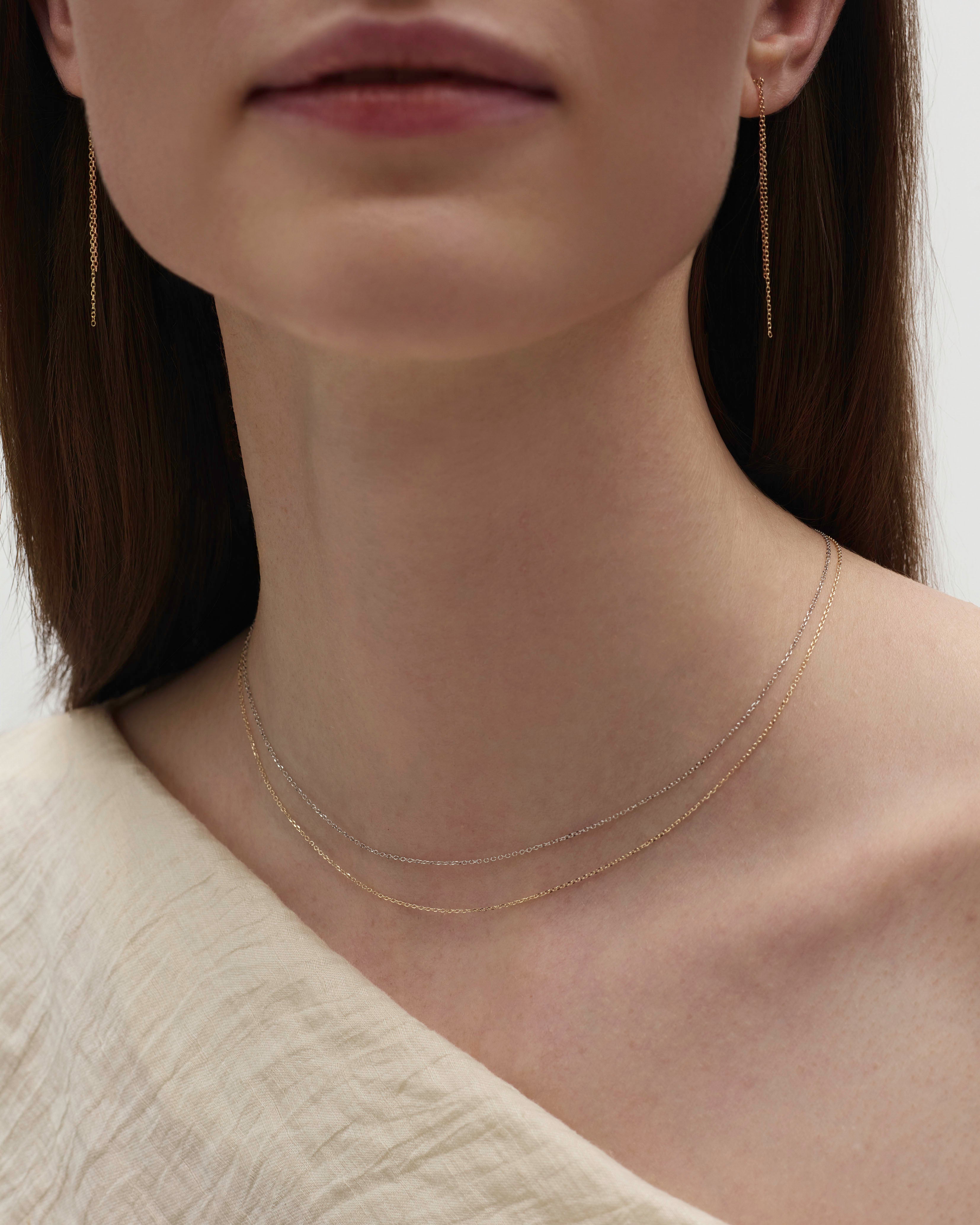 Delicate mixed metal 14K gold layered necklace on collarbone.