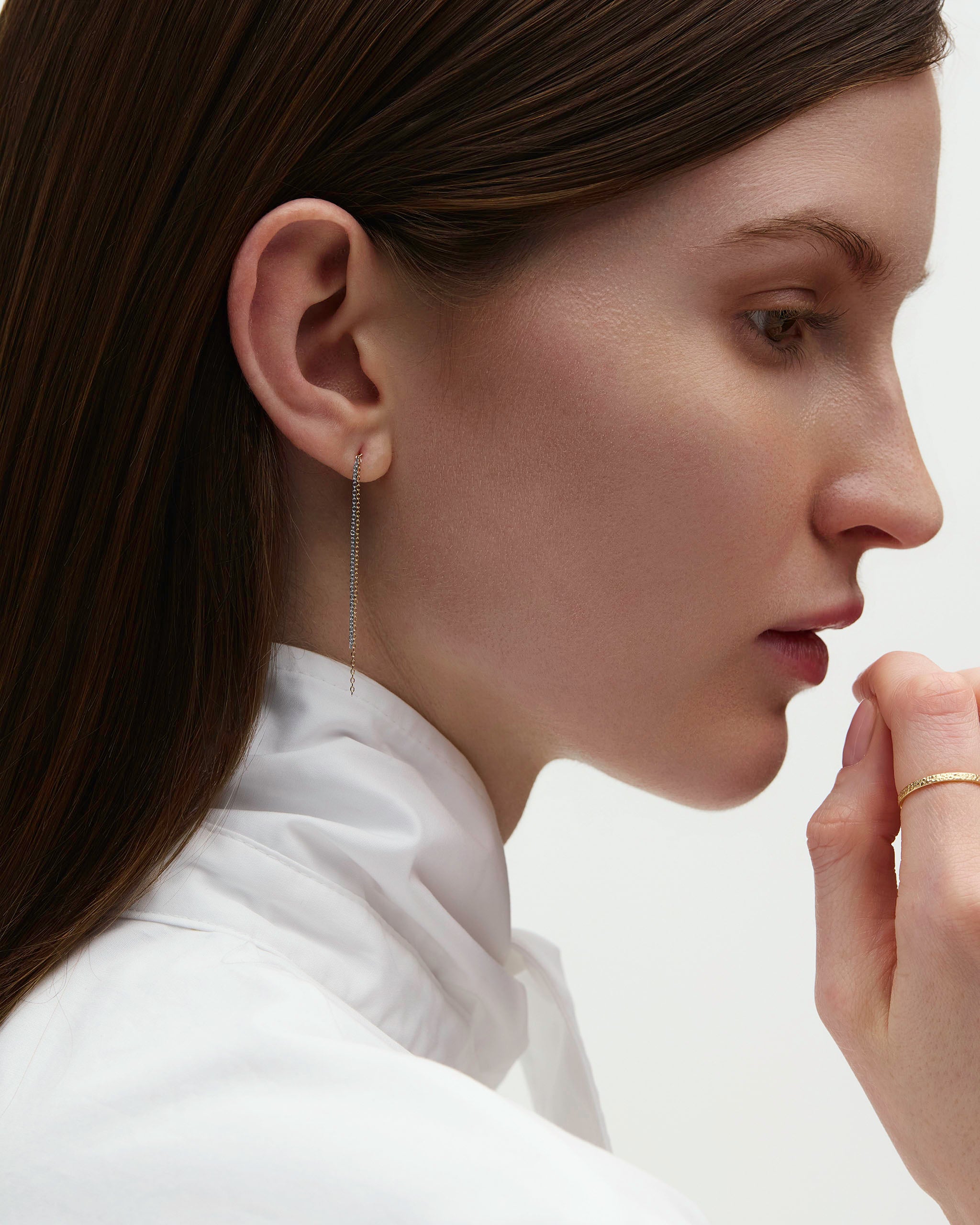 Side profile of model wearing Dyo Drop Chain Earrings against white collar.