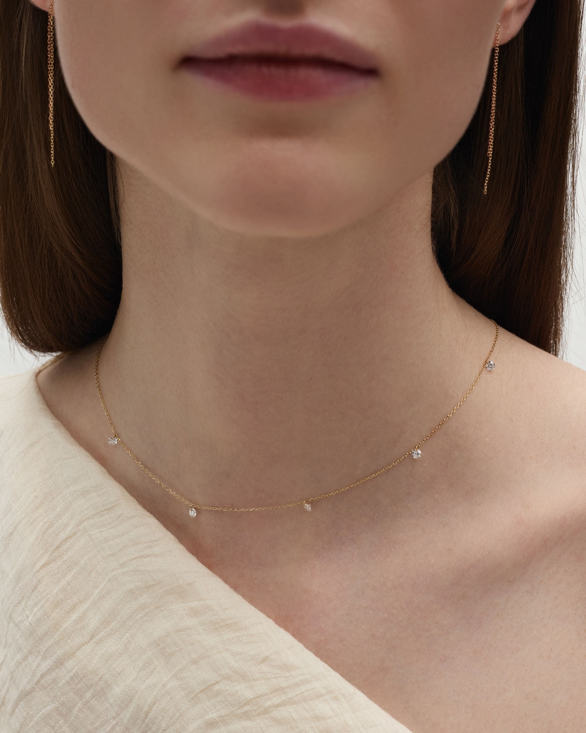 Close-up of a woman wearing solid gold nude diamond by the yard necklace on neckline showing dainty floating diamonds. Enea Studio