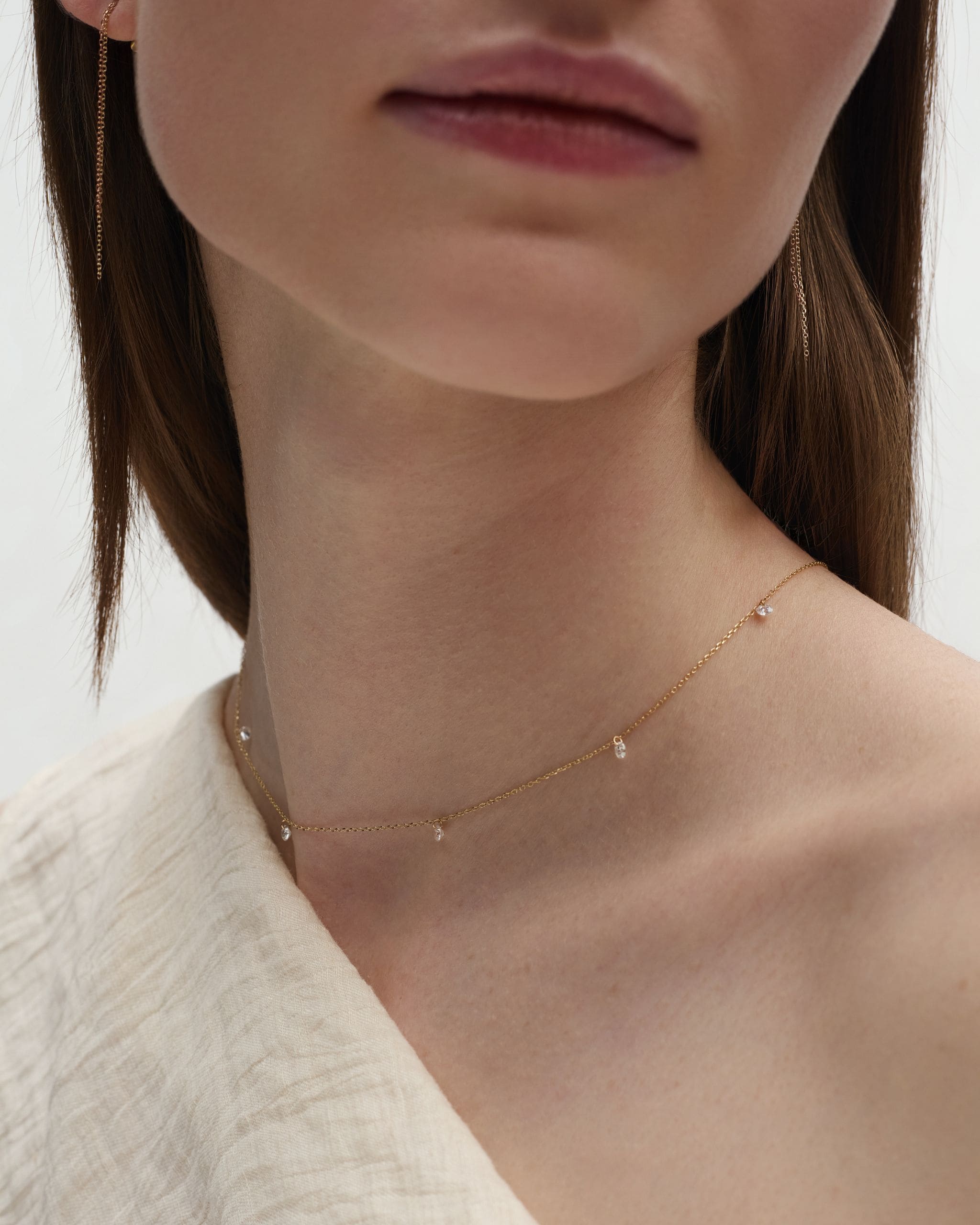 Close-up of a woman's neck styled with a solid gold nude diamond by the yard necklace featuring five pierced diamonds. Enea Studio