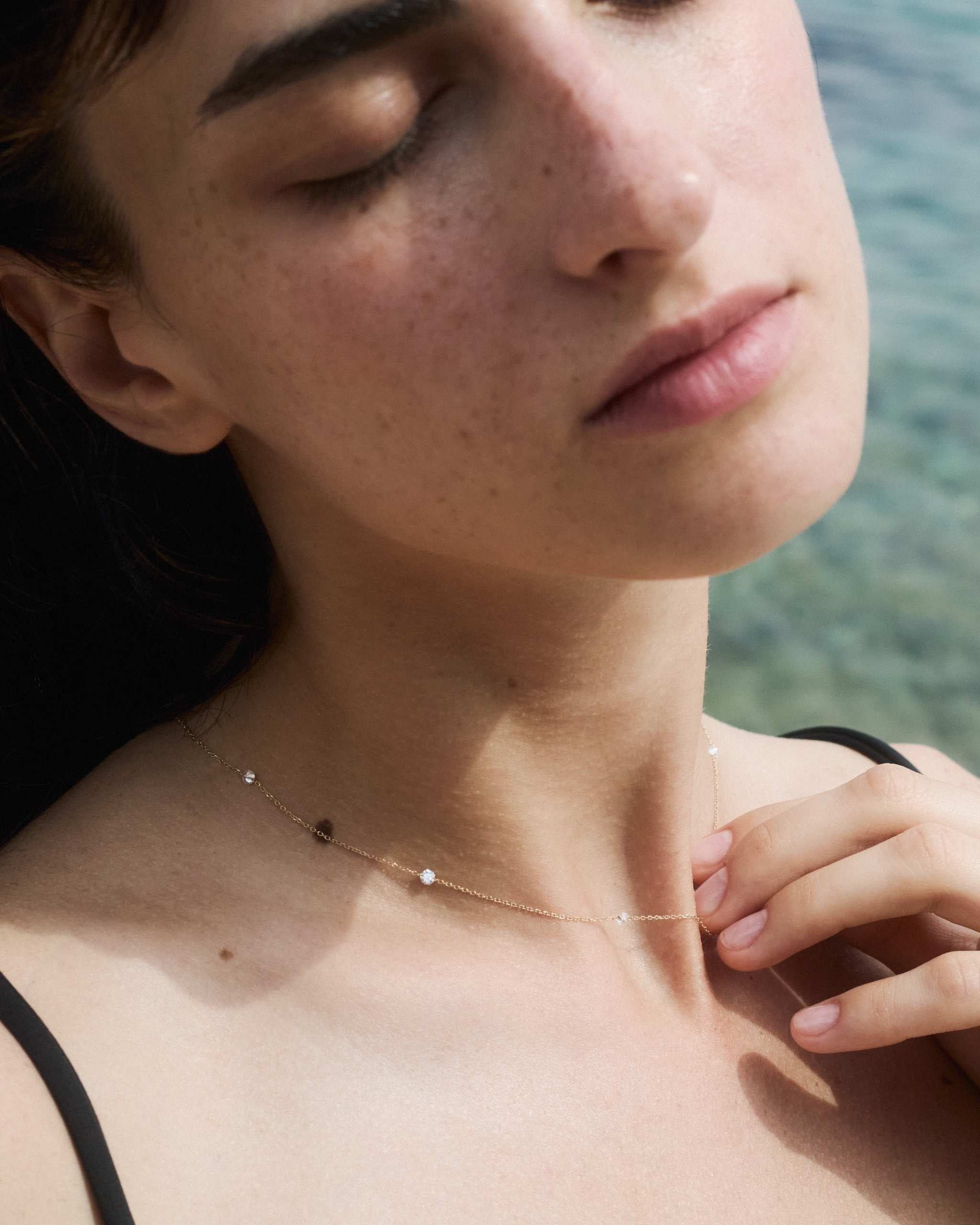 a woman wearing a solid gold diamond station necklace with four diamonds on a calm sea background