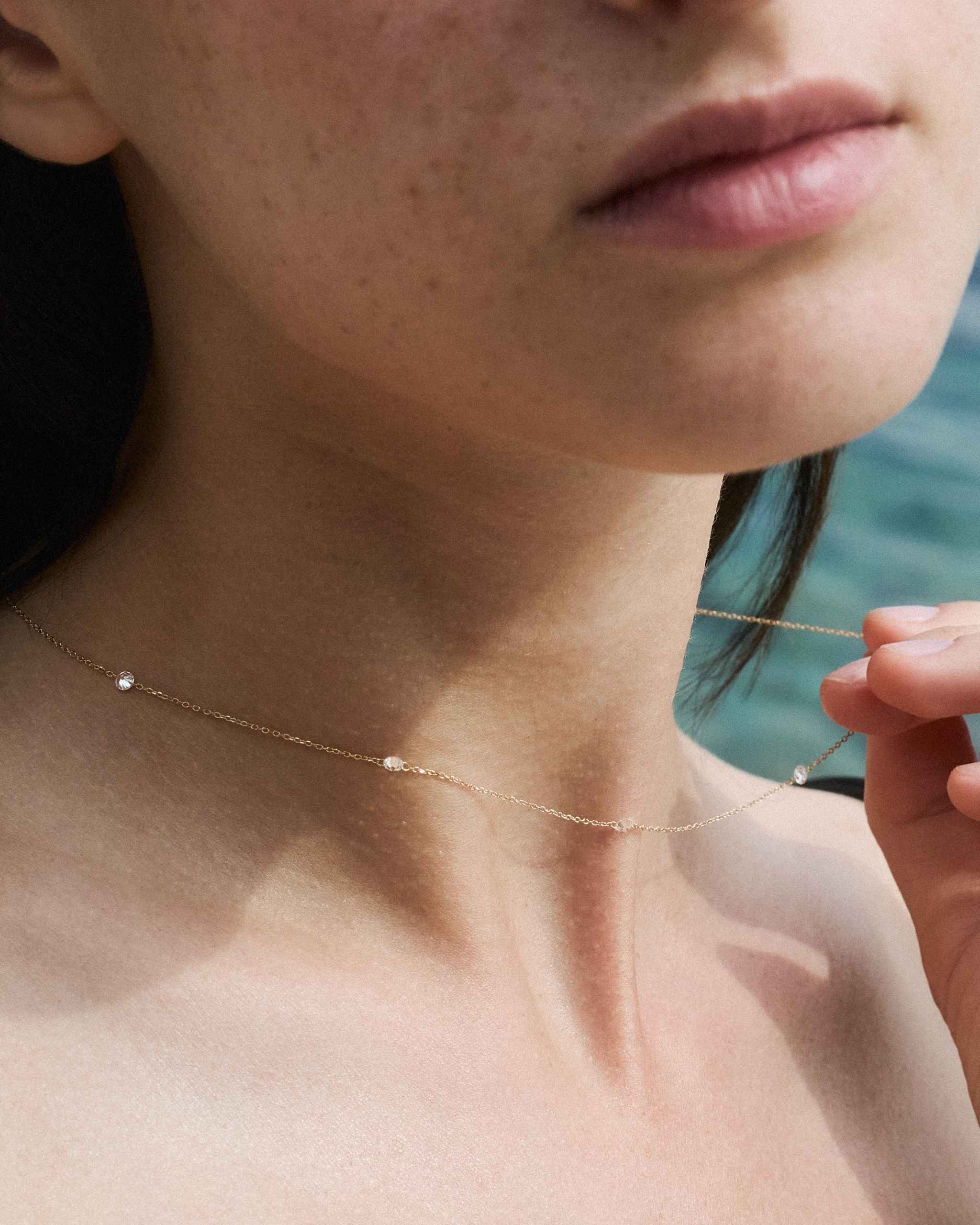 close up of a woman's neck wearing a solid gold diamond station necklace with four diamonds on a sea background