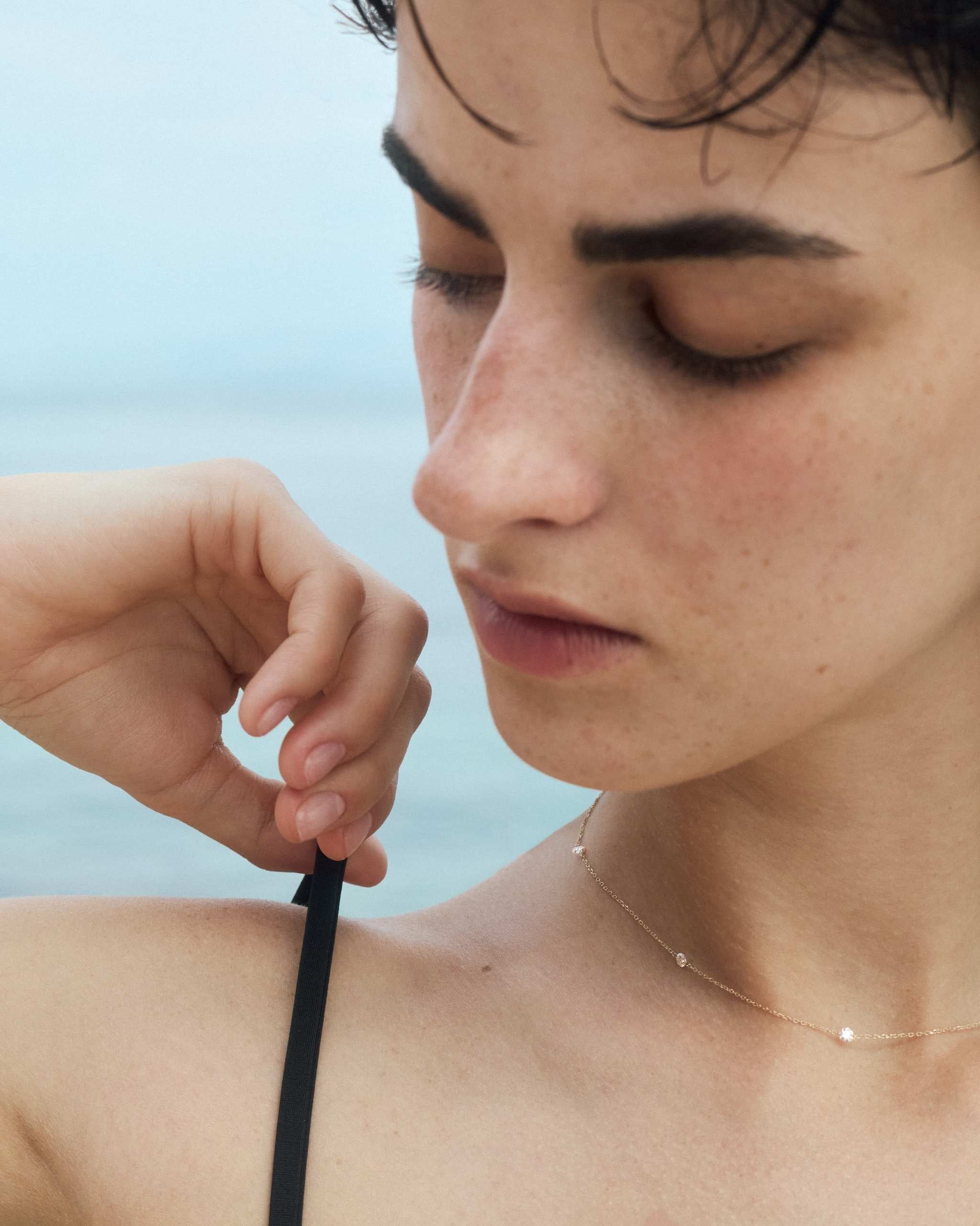 a woman wearing a solid gold diamond station necklace with four diamonds on a sea background
