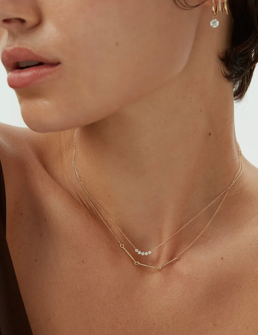 Close-up view of a woman wearing a 14k yellow gold Iris Necklace with bar and loop detail, layered with a diamond dot necklace.