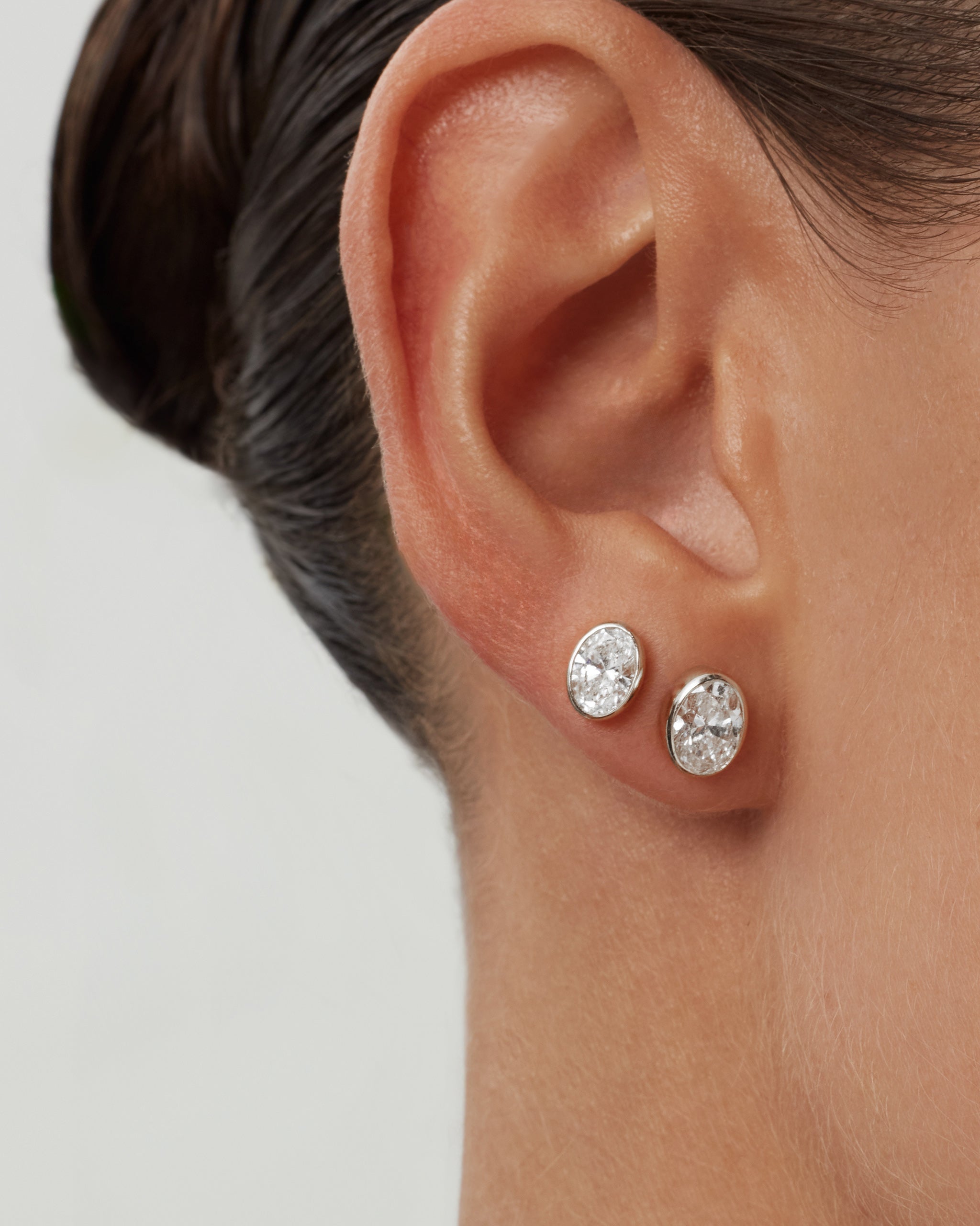 Model wearing oval bezel diamond stud earrings in 14k white gold on the lobe and second piercing, ENEA Studio