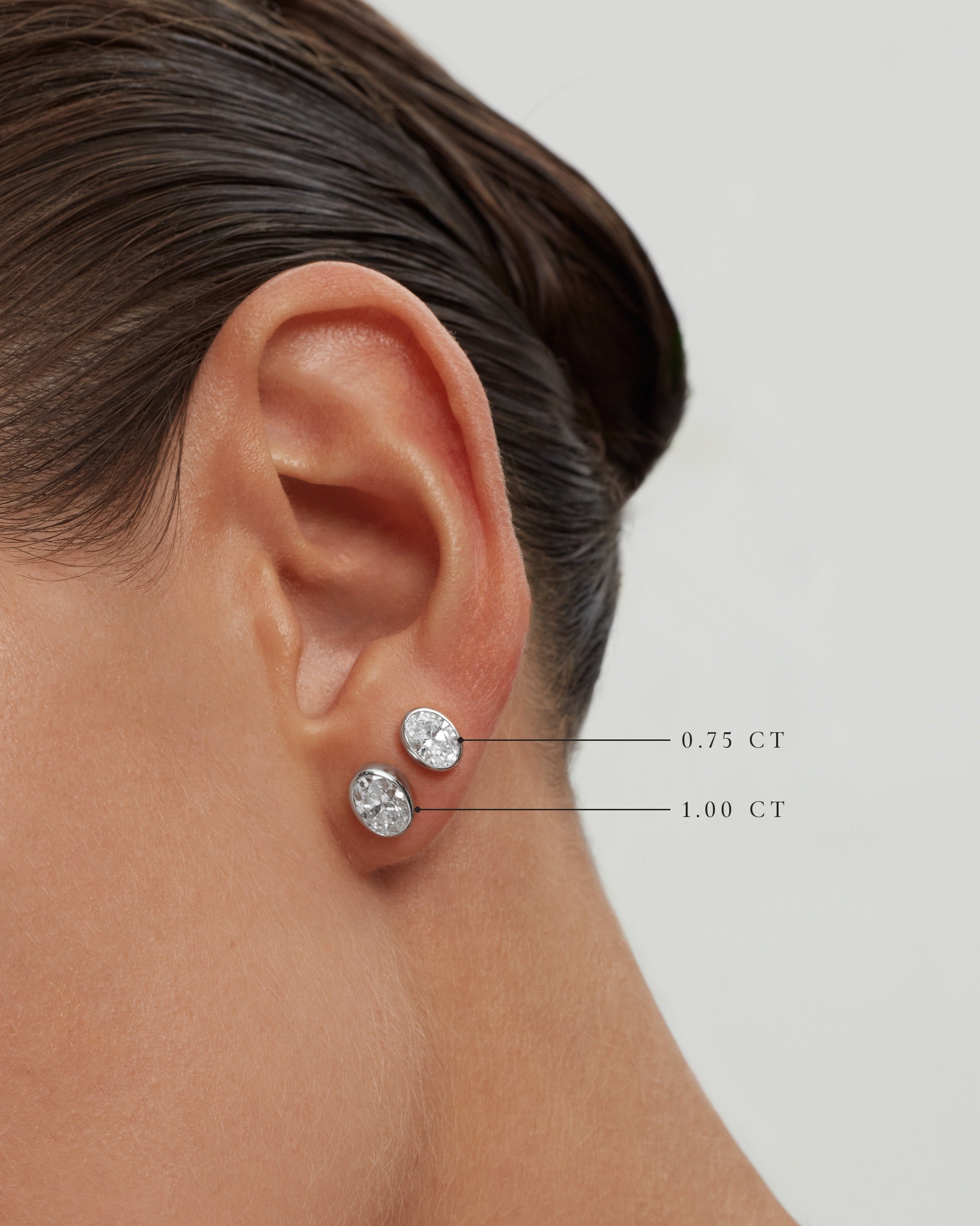 Model wearing oval bezel diamond studs in 14k white gold, 0.75 ct and 1.00 ct each, labelled, ENEA Studio