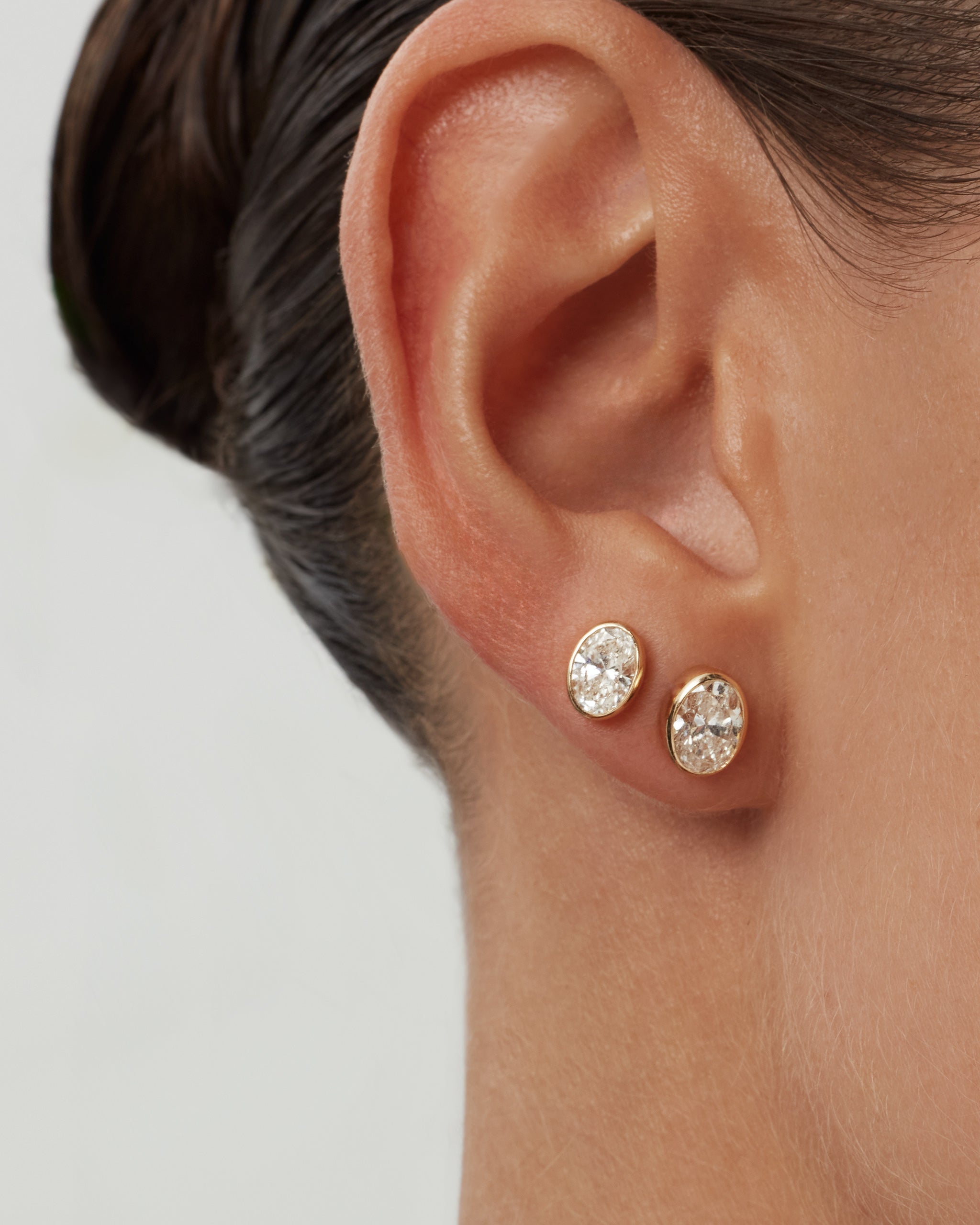Model wearing oval bezel diamond stud earrings in 14k yellow gold on the lobe and second piercing, ENEA Studio