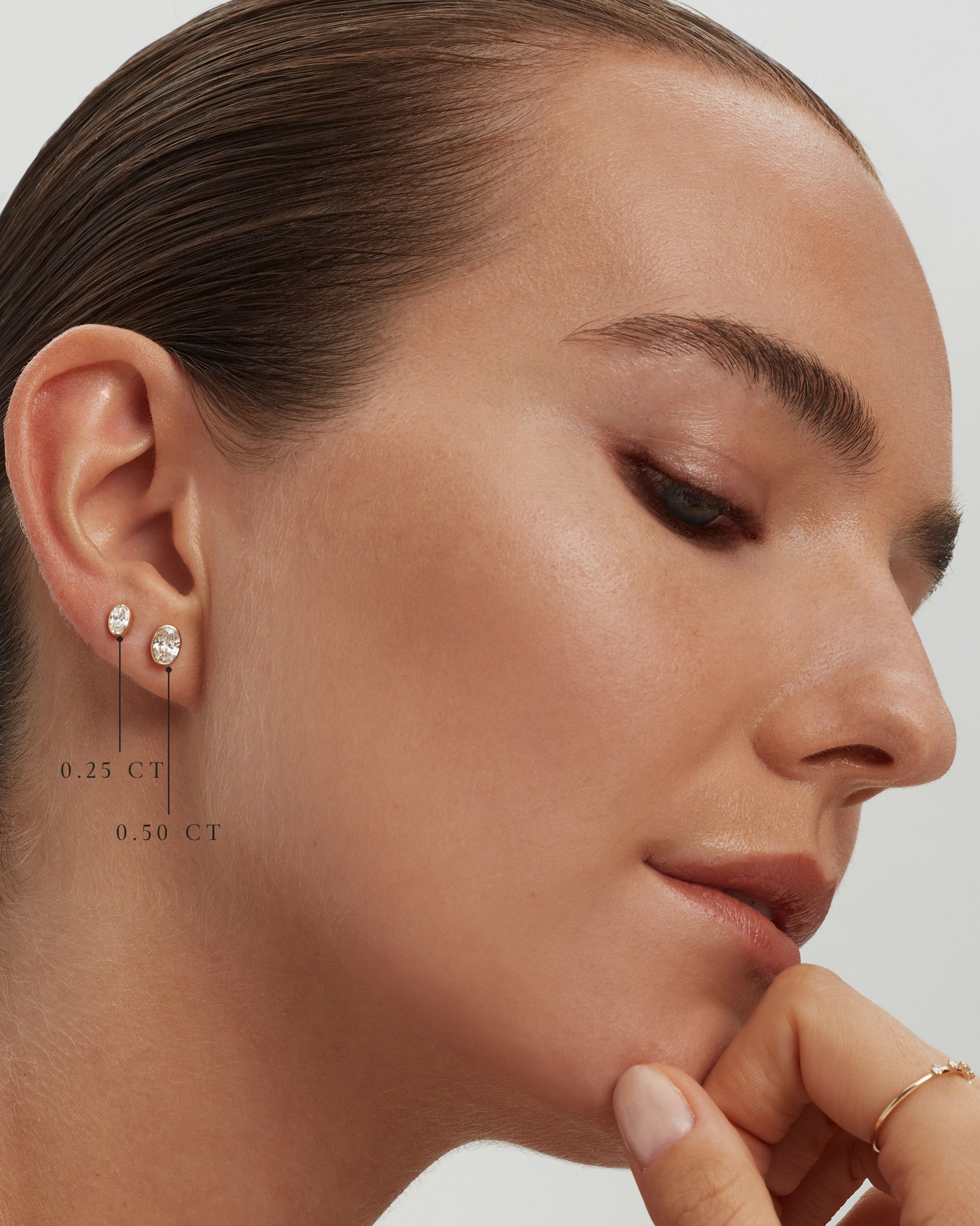 Model wearing oval bezel diamond studs in 14k yellow gold, 0.25 ct and 0.50 ct each, labelled, ENEA Studio