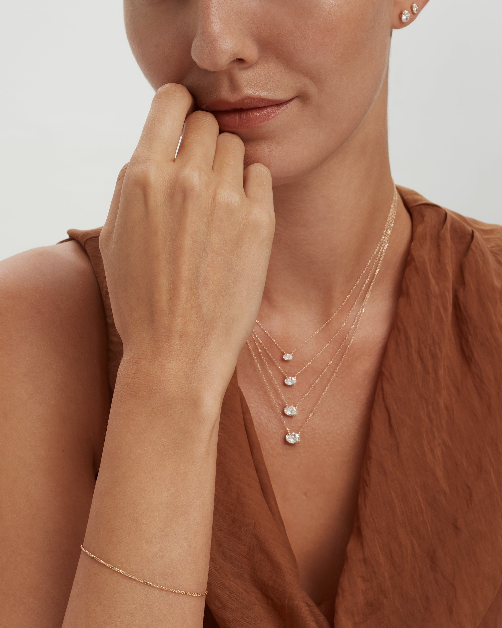 Model wearing oval diamond necklaces layered with oval diamond studs, shown in 14k yellow gold, ENEA Studio