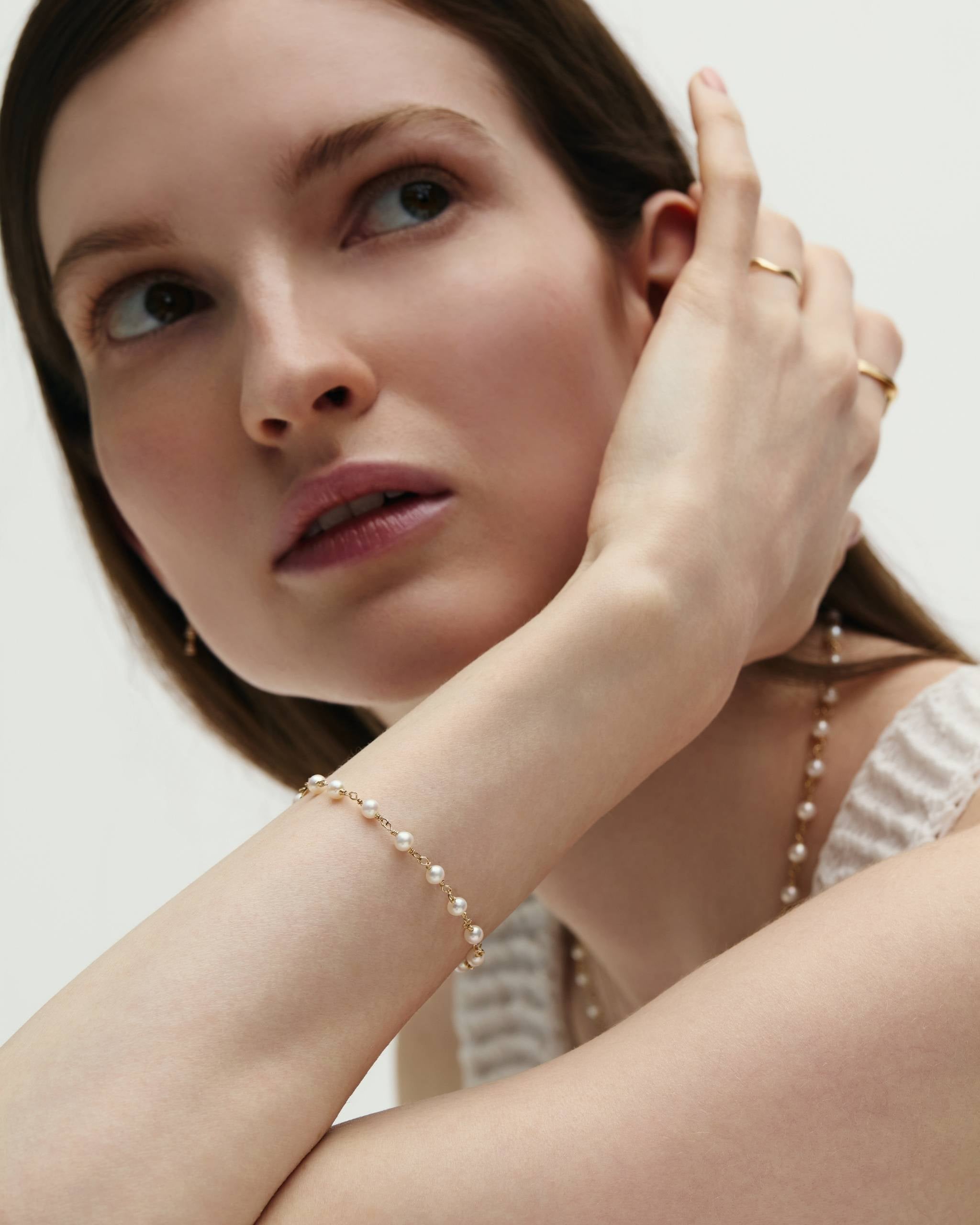 A woman resting her hand on her face with her wrist styled with a 14k Gold Pearl Wrap Bracelet