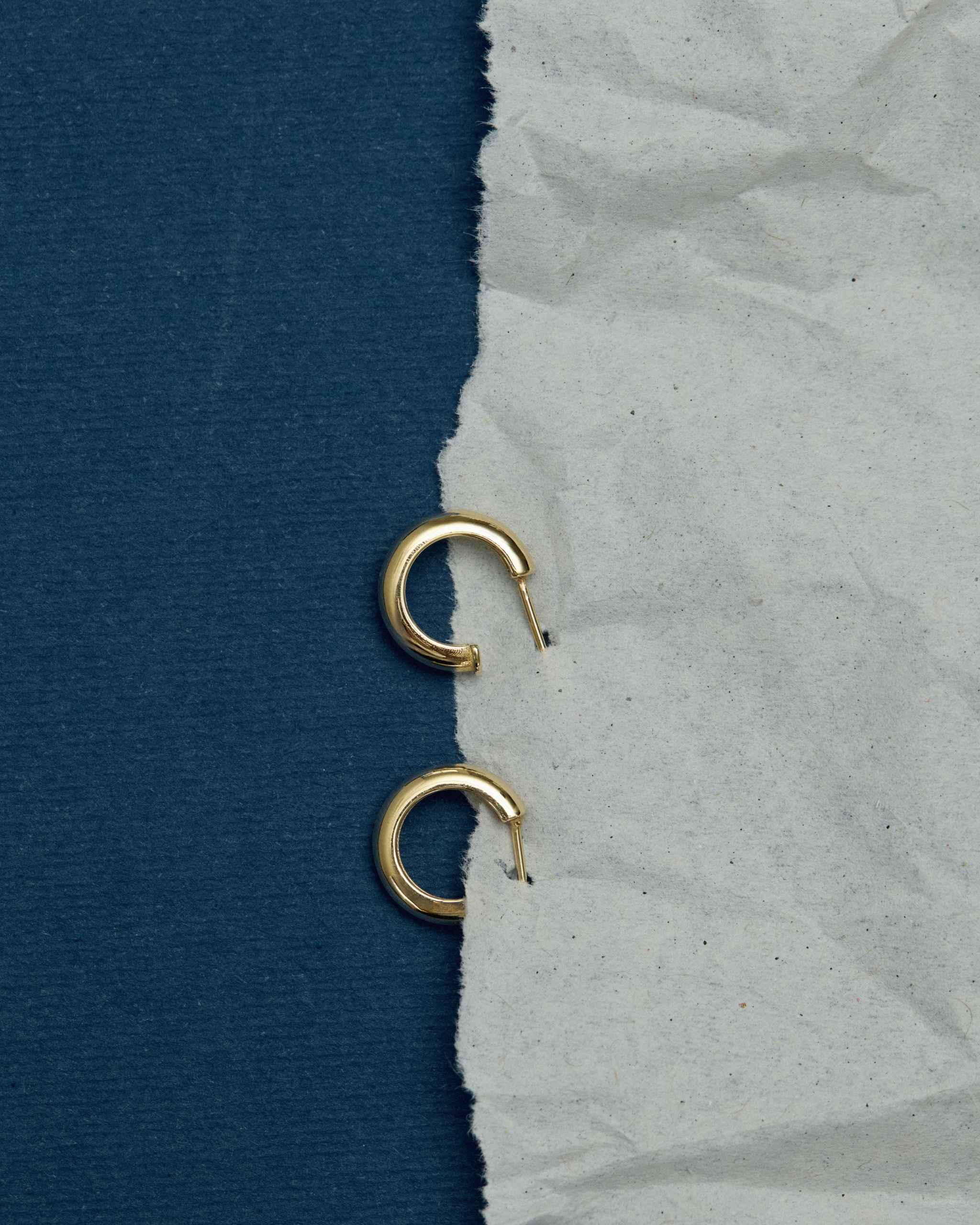 upper view of a polished pair of solid gold stud hoops on white crumpled paper on blue background