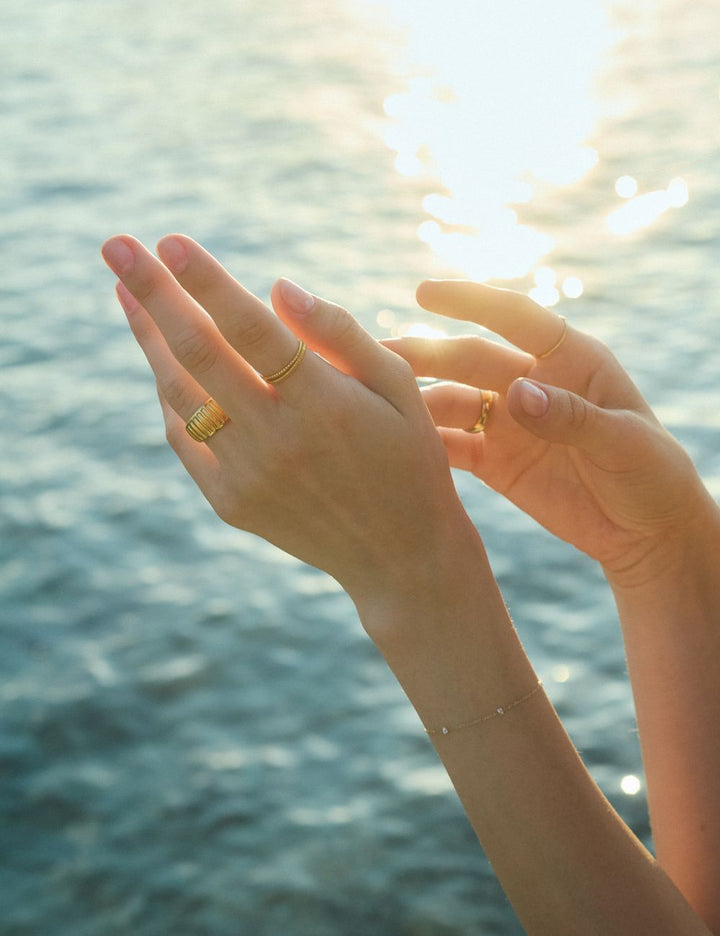 Hands with gold rings in sunlight over the sea, ENEA Studio