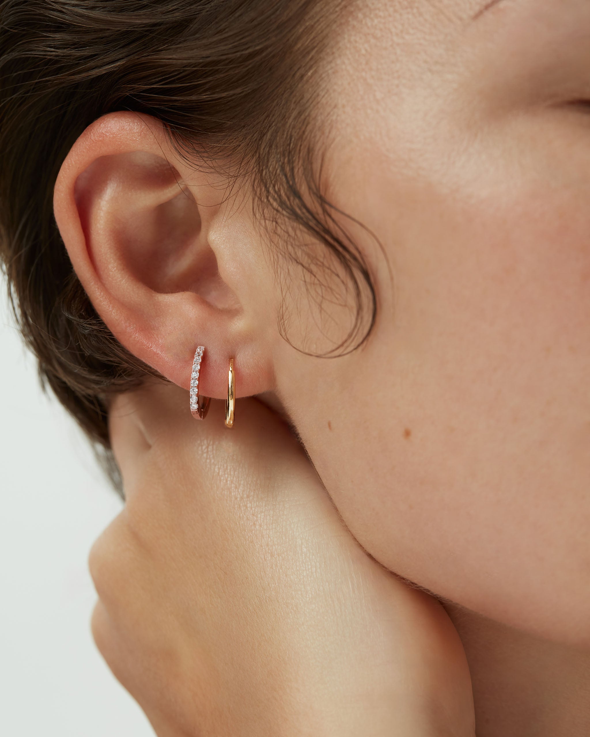 14k rose gold huggie earring stack with diamond pavé huggie and plain gold huggie hoop worn together on model