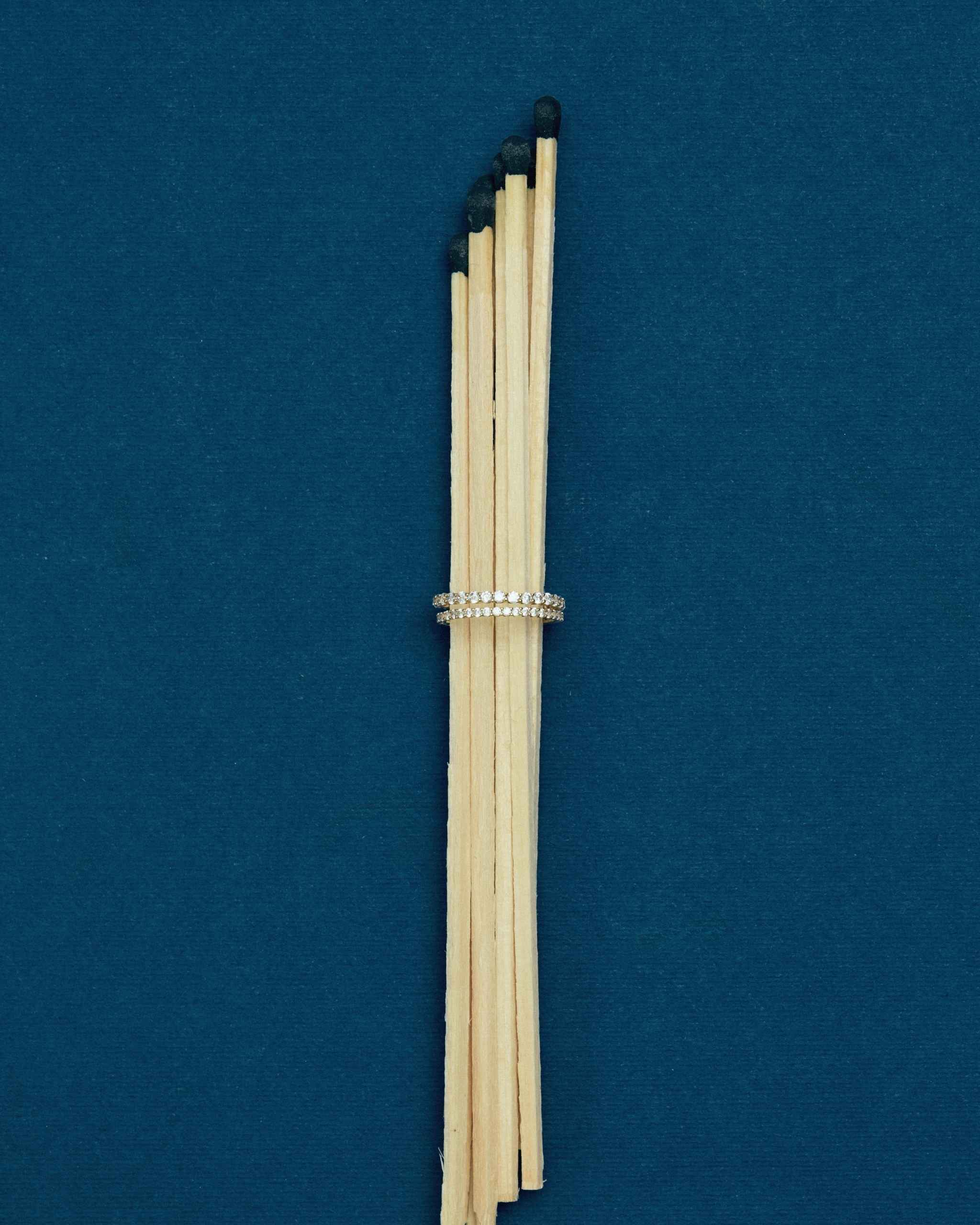 a bundle of matches passed through two diamond eternity rings in different widths on a blue surface
