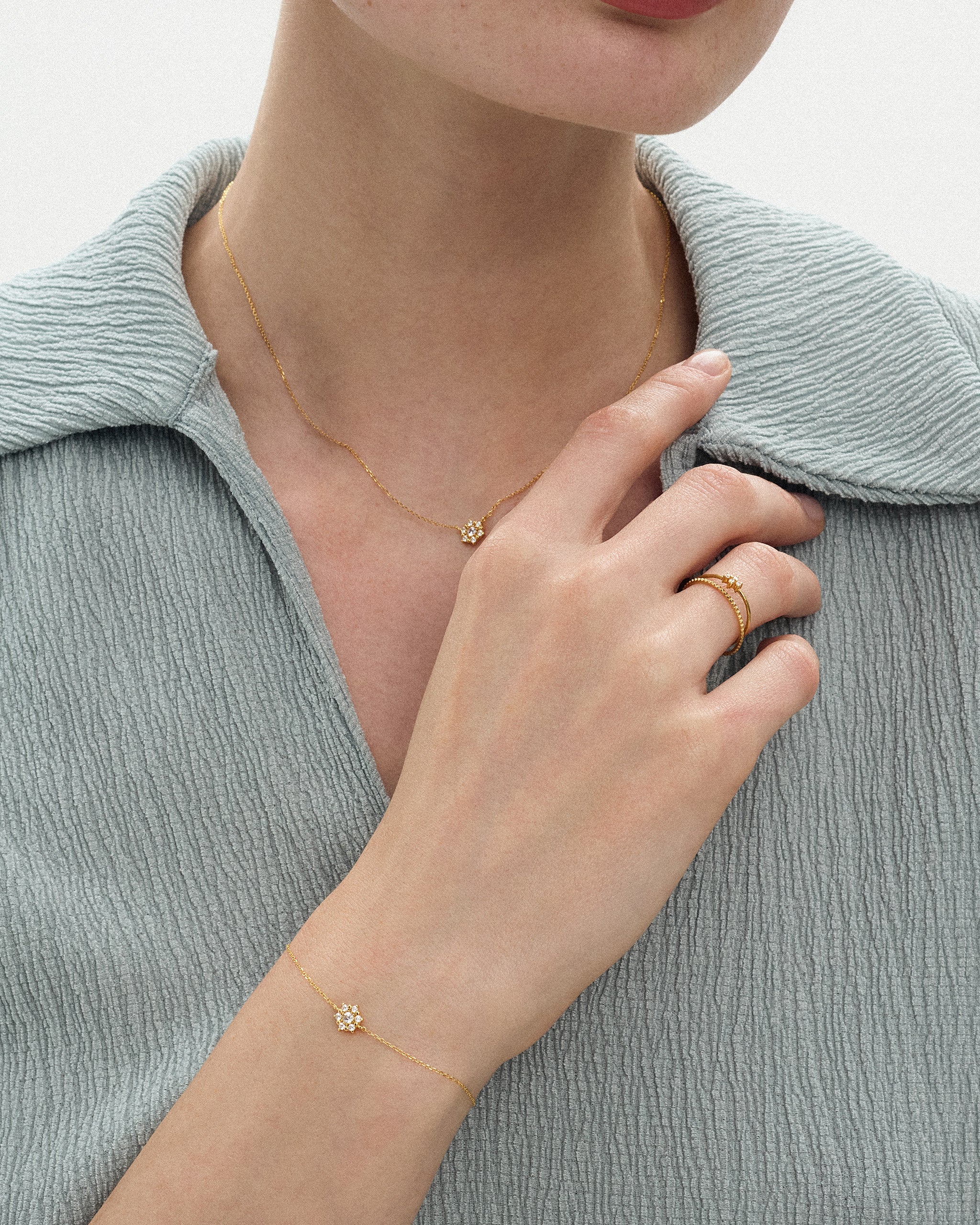Woman wearing the Selas Diamond Cluster Bracelet in 14k yellow gold on her wrist with the matching Selas Diamond Necklace, hand resting at her collar. ENEA Studio
