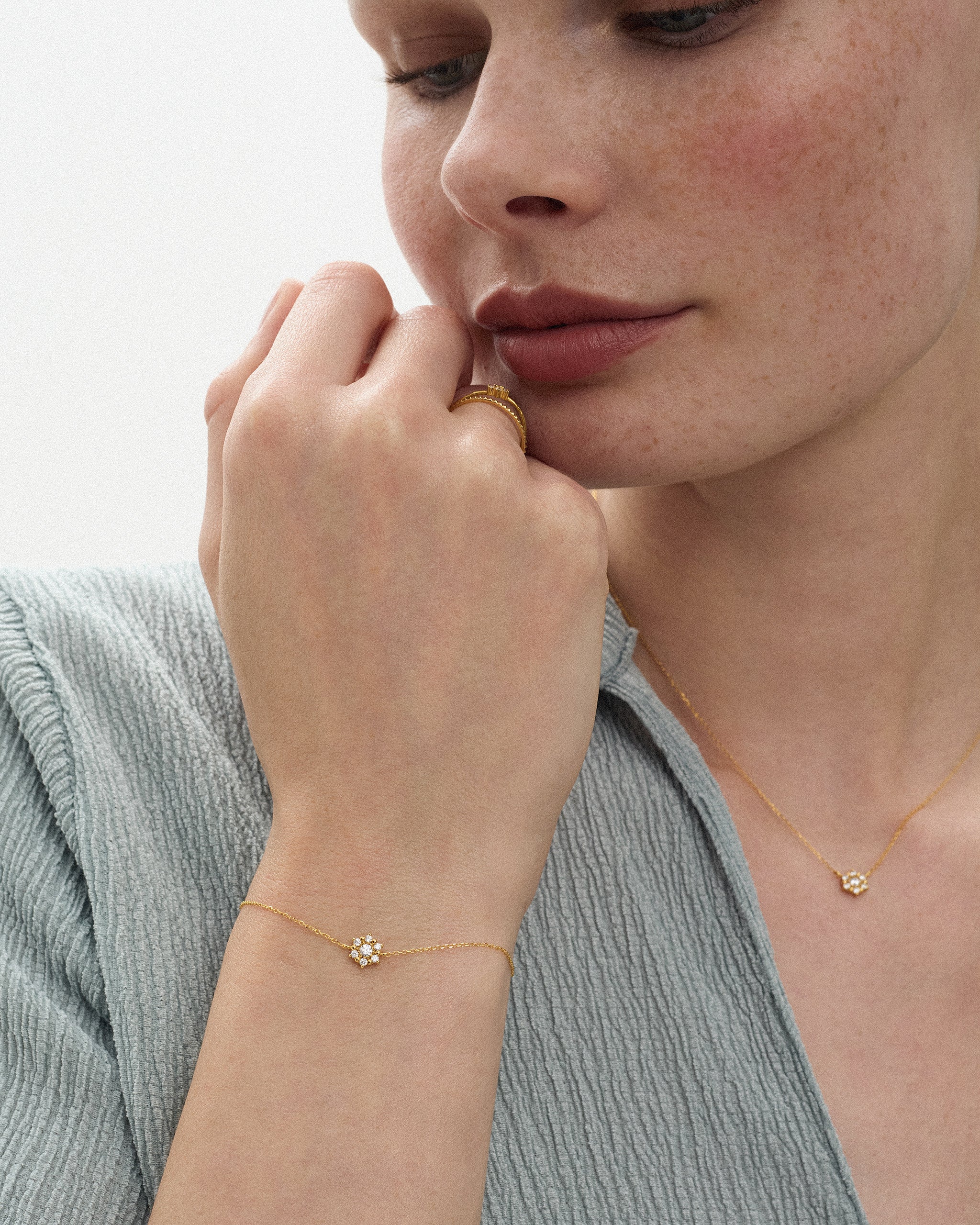 Close up of a woman wearing the Selas Diamond Cluster Bracelet in 14k yellow gold, hand raised to her chin, with the Selas Diamond Necklace at her collarbone. ENEA Studio