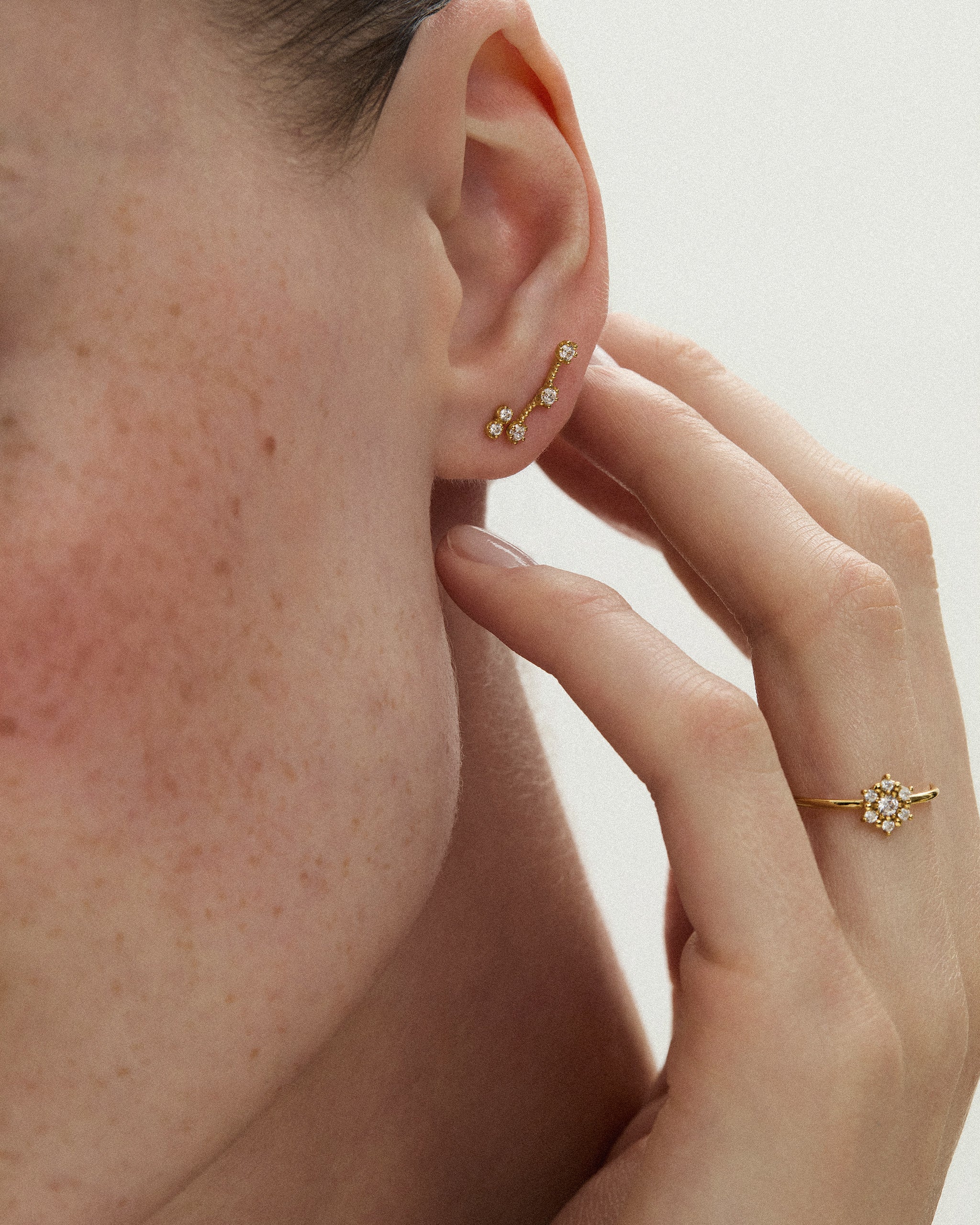Woman wearing the Selas Diamond Cluster Ring in 14k yellow gold with the Celestial Diamond Climber Earrings, hand resting near her ear. ENEA Studio