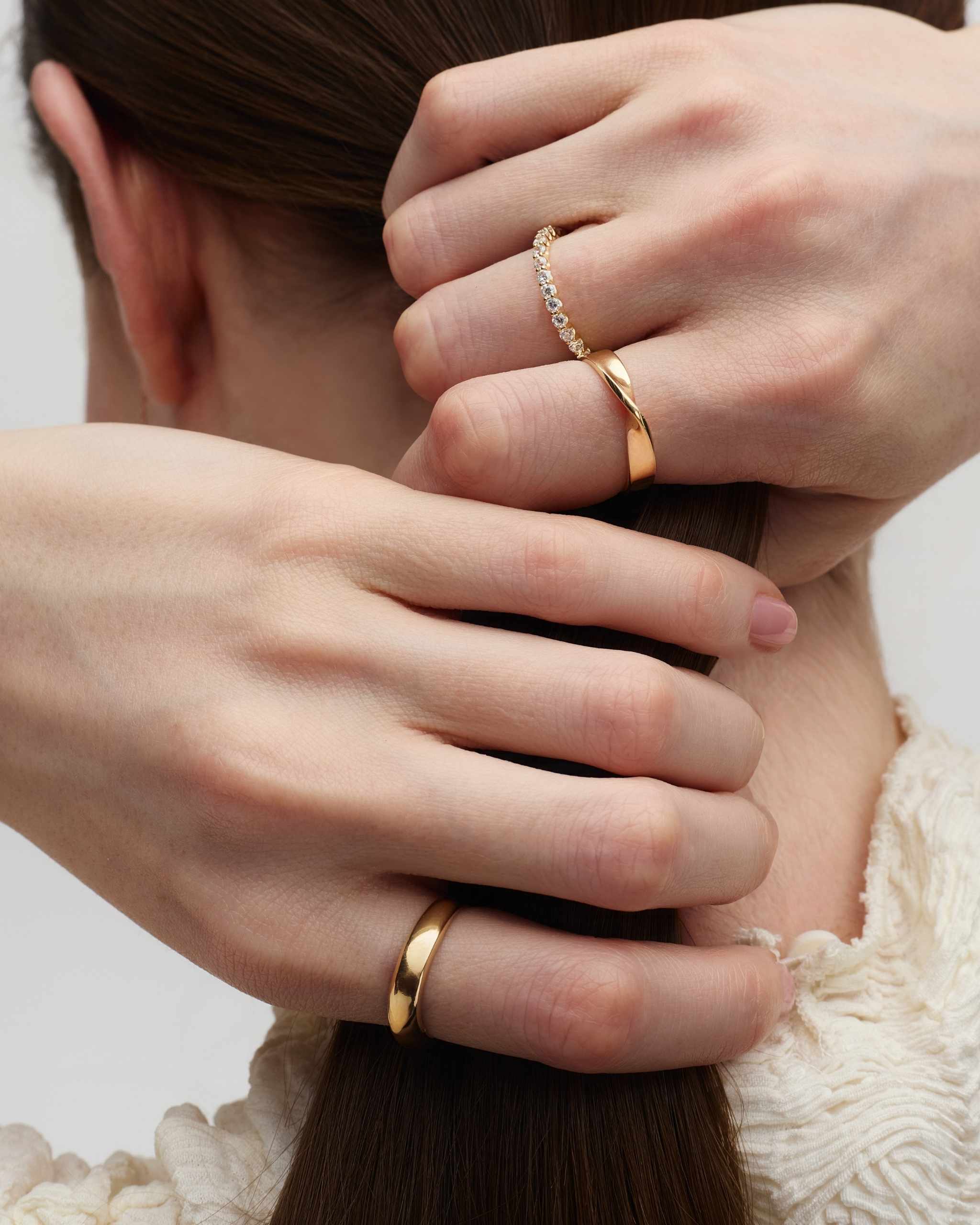 back view of a woman holding her ponytail with her hands accesorized with plain solid gold bands and a diamond eternity ring