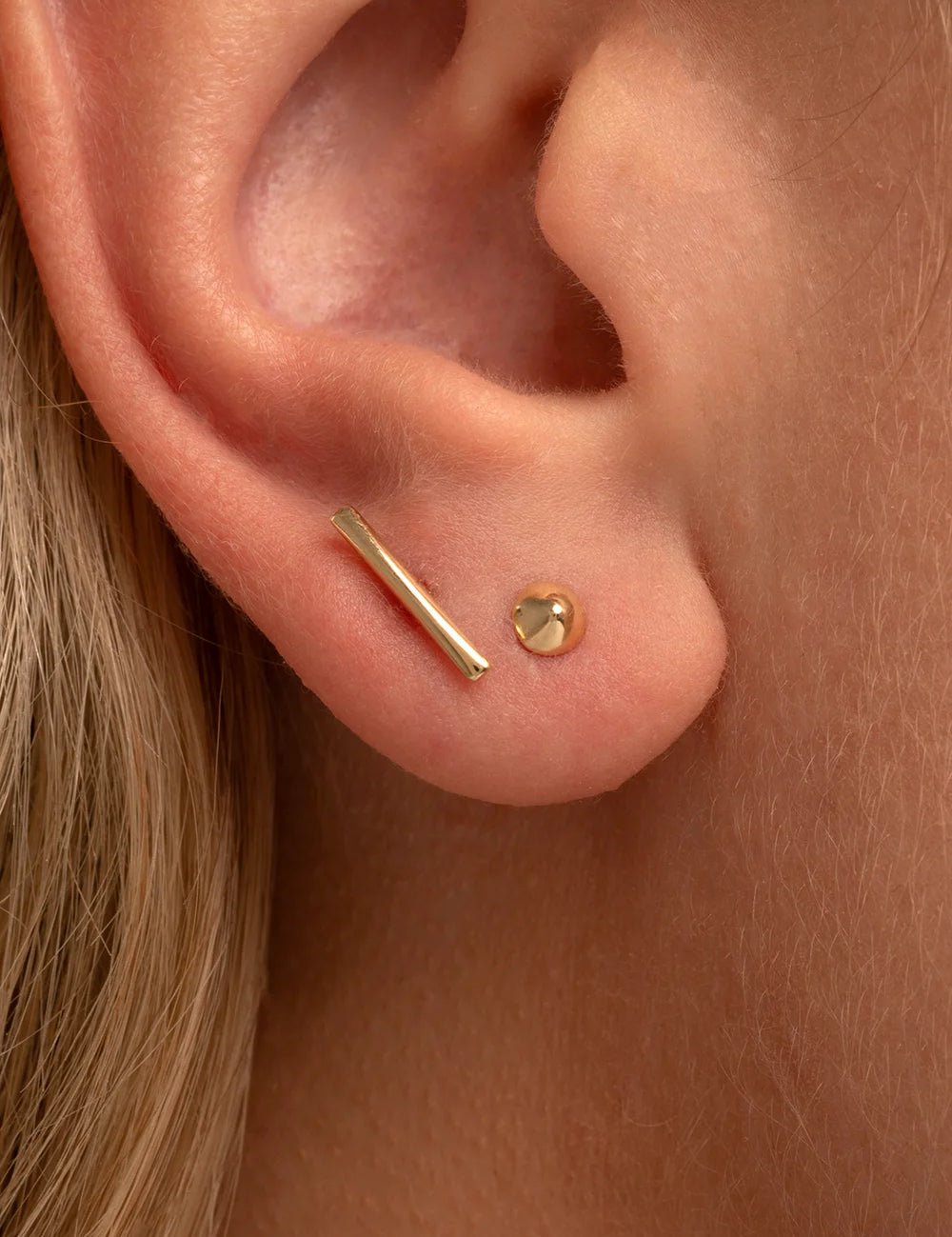 Close-up of a model wearing a single yellow gold stud earring in her helix piercing.