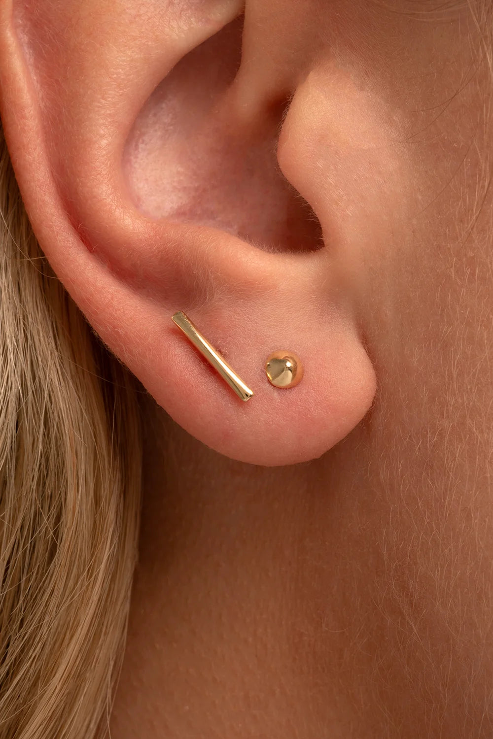 Close-up of a model wearing a single yellow gold stud earring in her helix piercing.