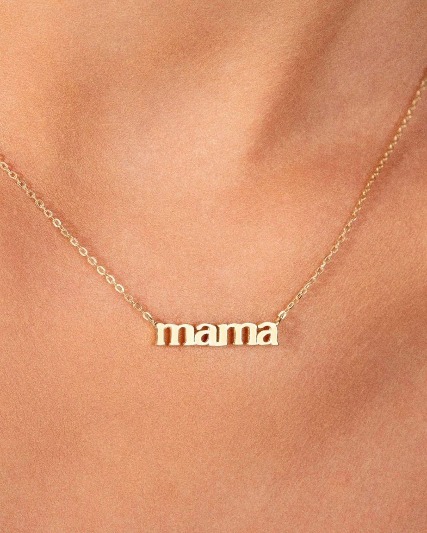 Gold 'mama' necklace on a person's neck against a neutral background, close up