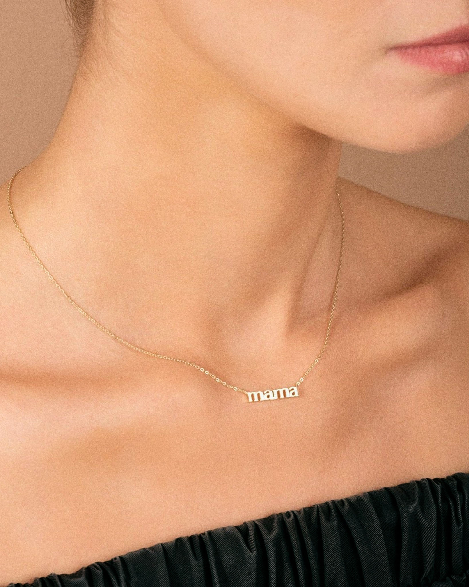 Gold 'mama' necklace on a person's neck with a neutral background angled view
