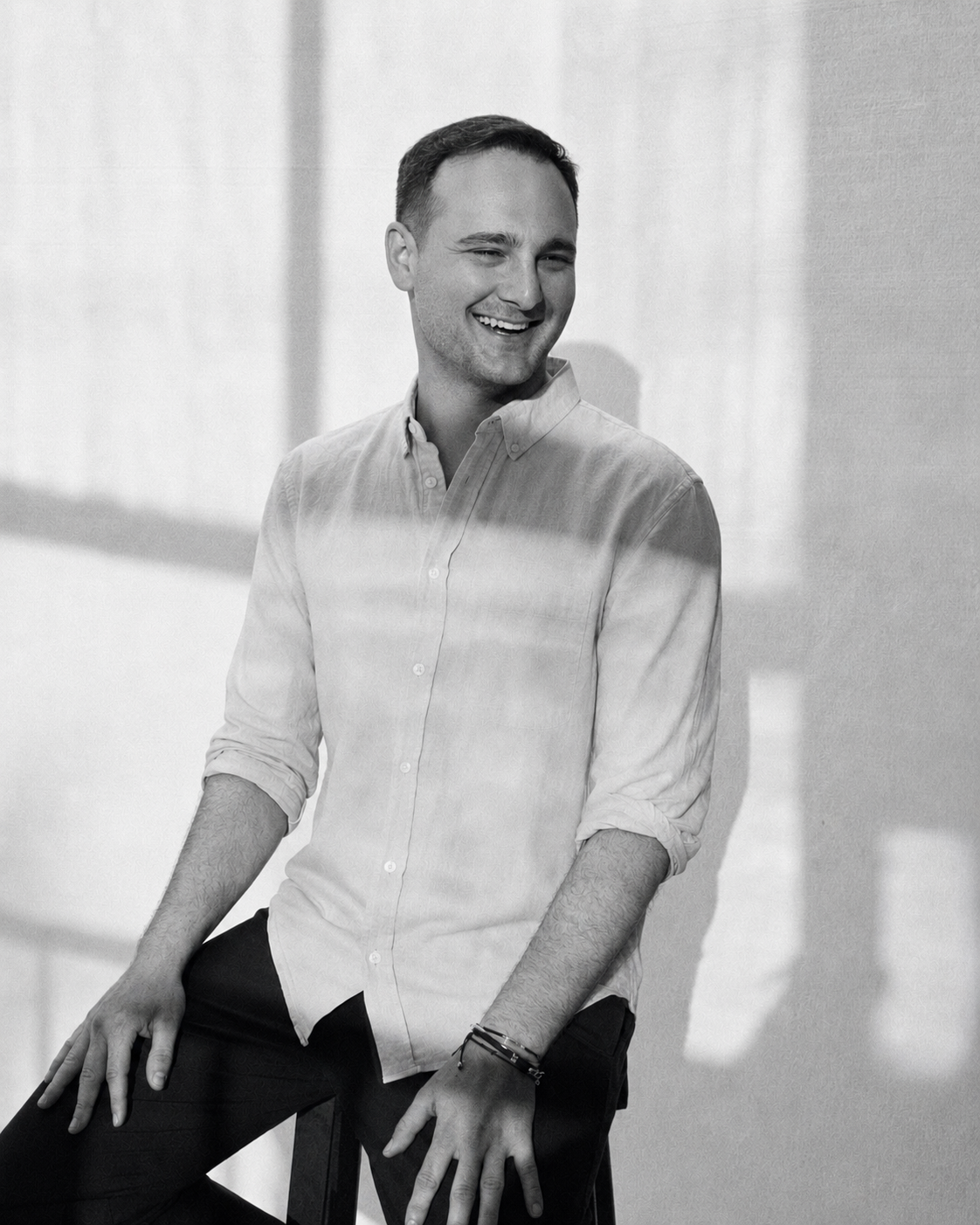 Laki, founder and CEO of ENEA, laughing in a black-and-white portrait, wearing a linen shirt against a sunlit wall.