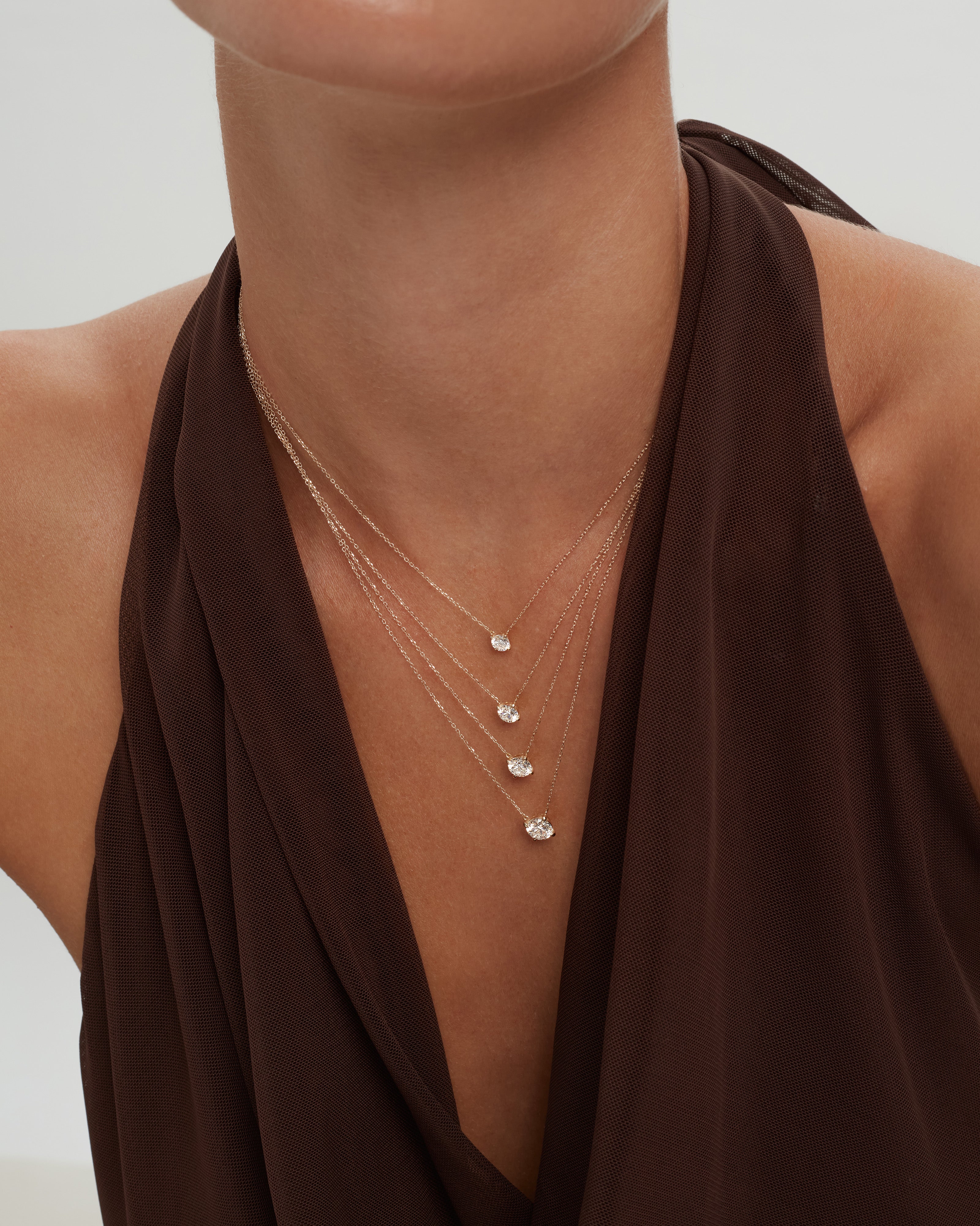 Close up of a woman's neck wearing Enea's Éclat Grand Diamond Solitaire Necklace in yellow gold layered in 4 different diamond sizes