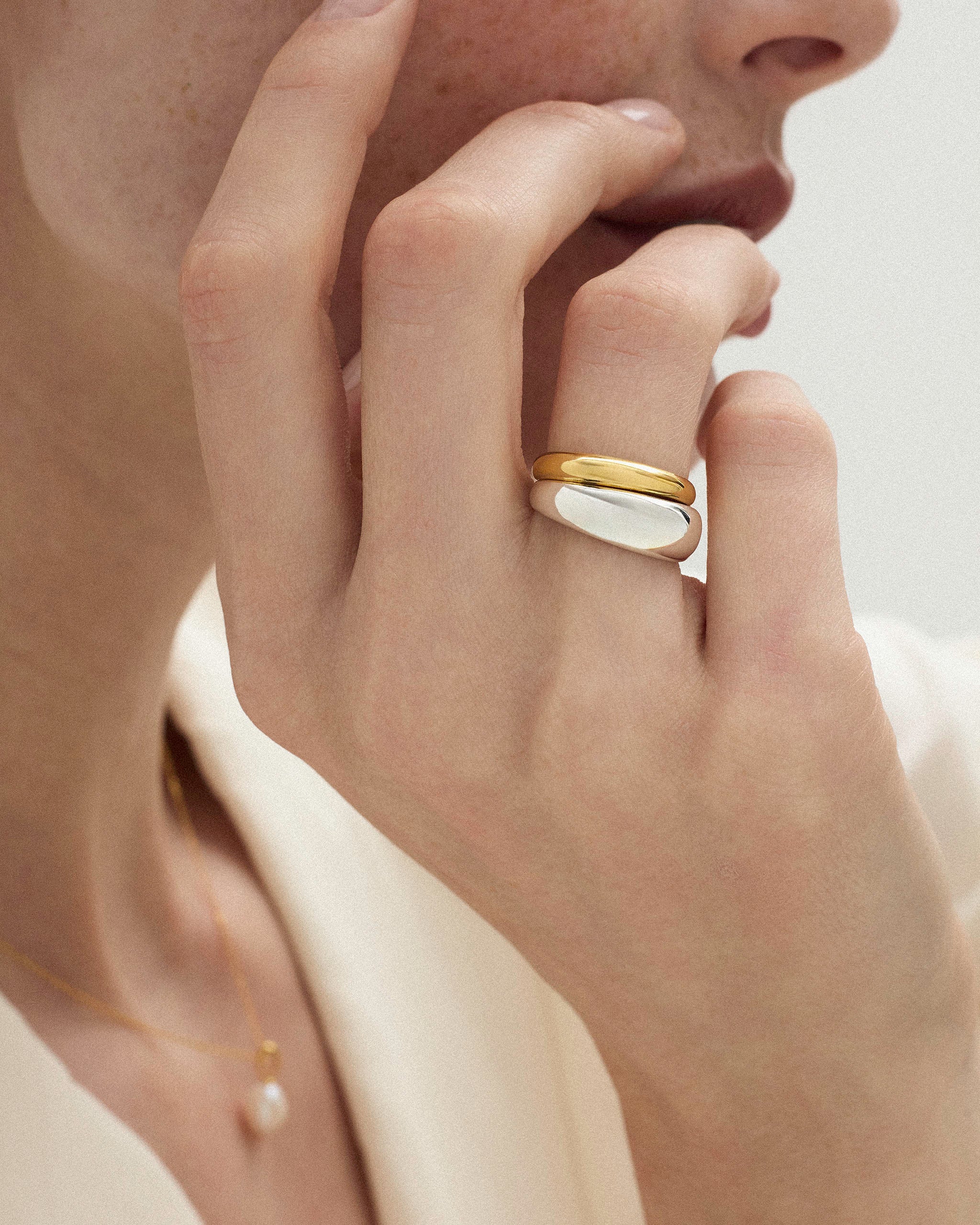 Hand resting against neck wearing DYO Dome Stacking Ring set in yellow gold and silver.