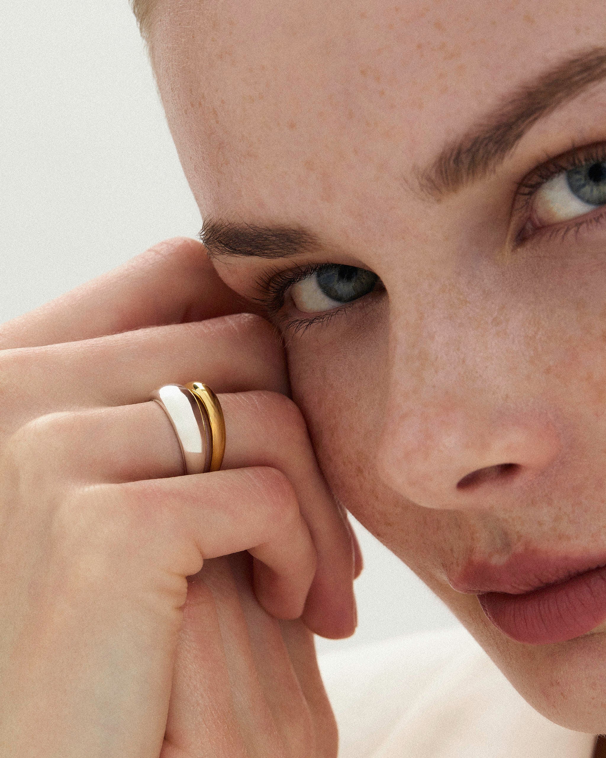 Model wears DYO Dome Stacking Ring set, 14k gold and sterling silver, close crop on hand near face.