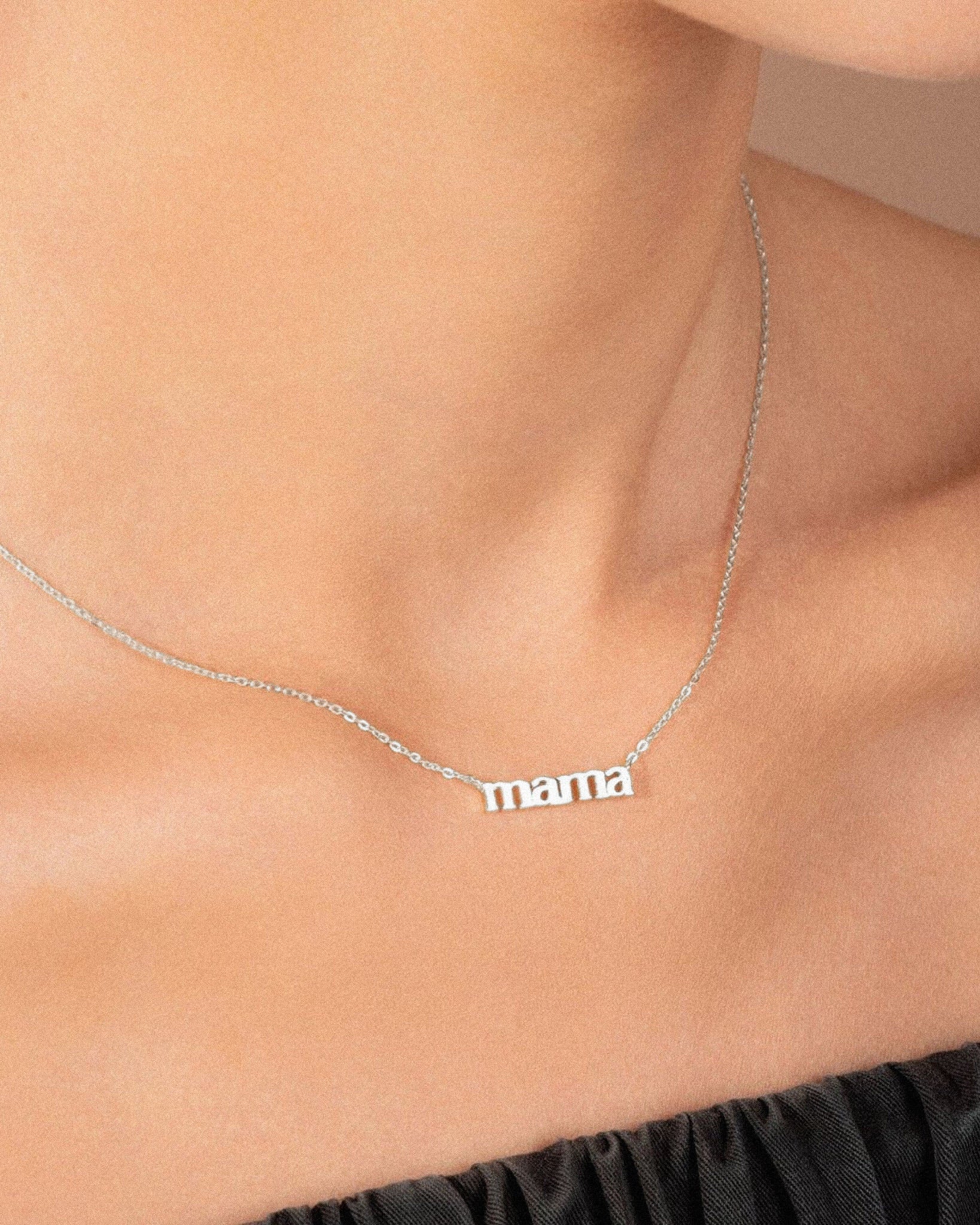 White gold 'mama' necklace on a person's neck against a neutral background