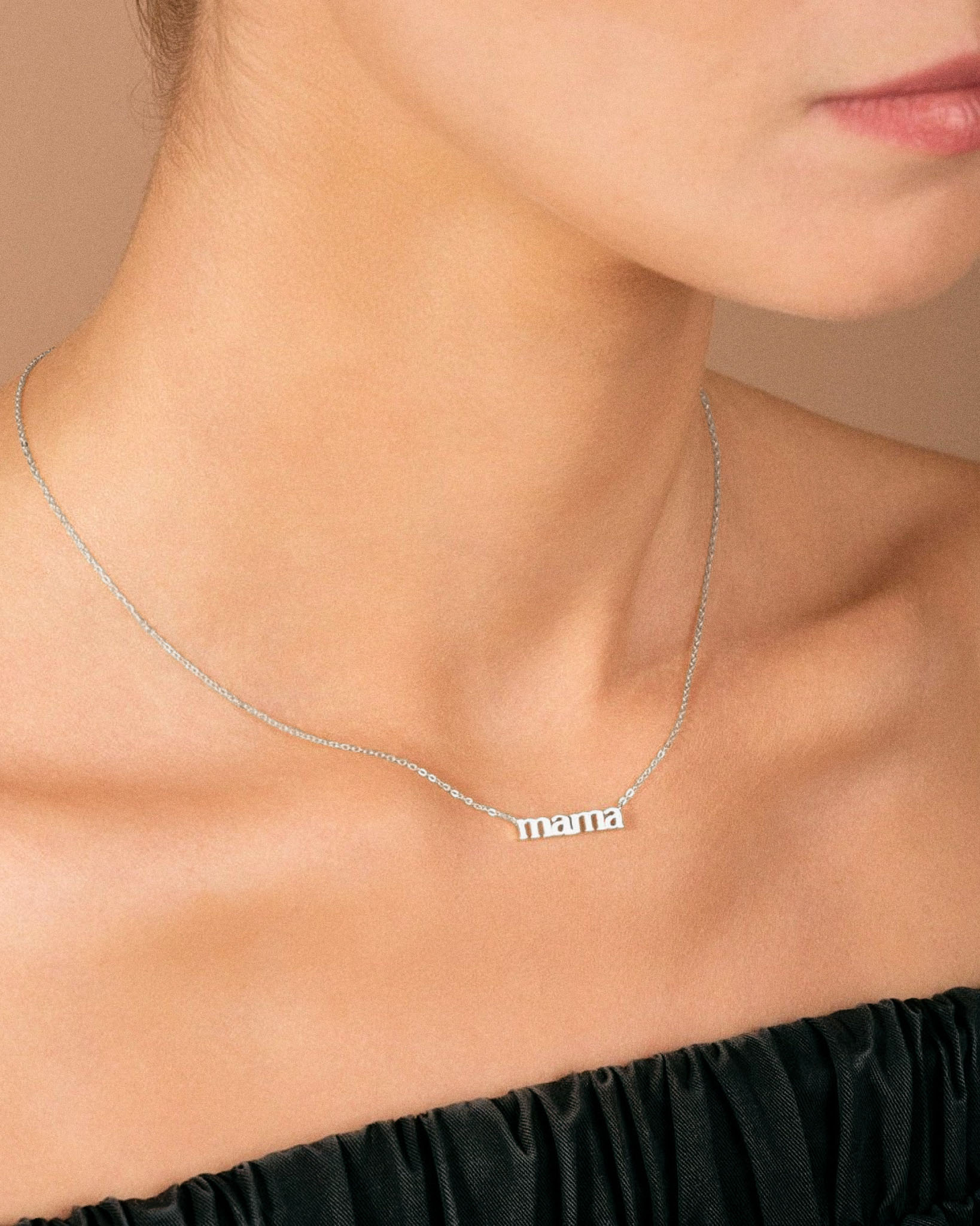 White gold 'mama' necklace on a person wearing a black top against a beige background
